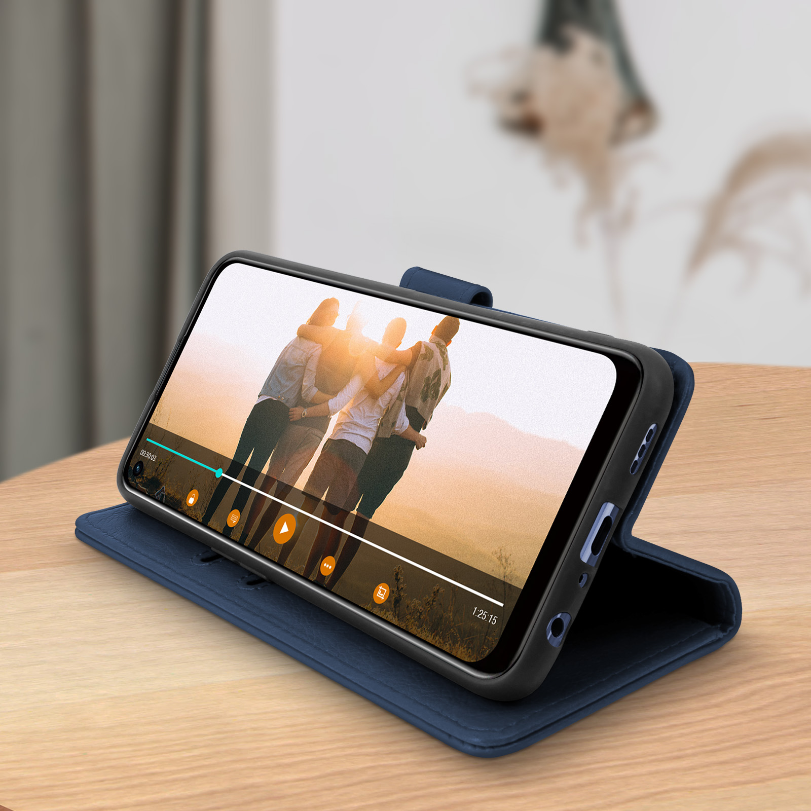 Un téléphone jouant une vidéo est dans un étui bleu, sur une surface en bois. Figures floues en arrière-plan.