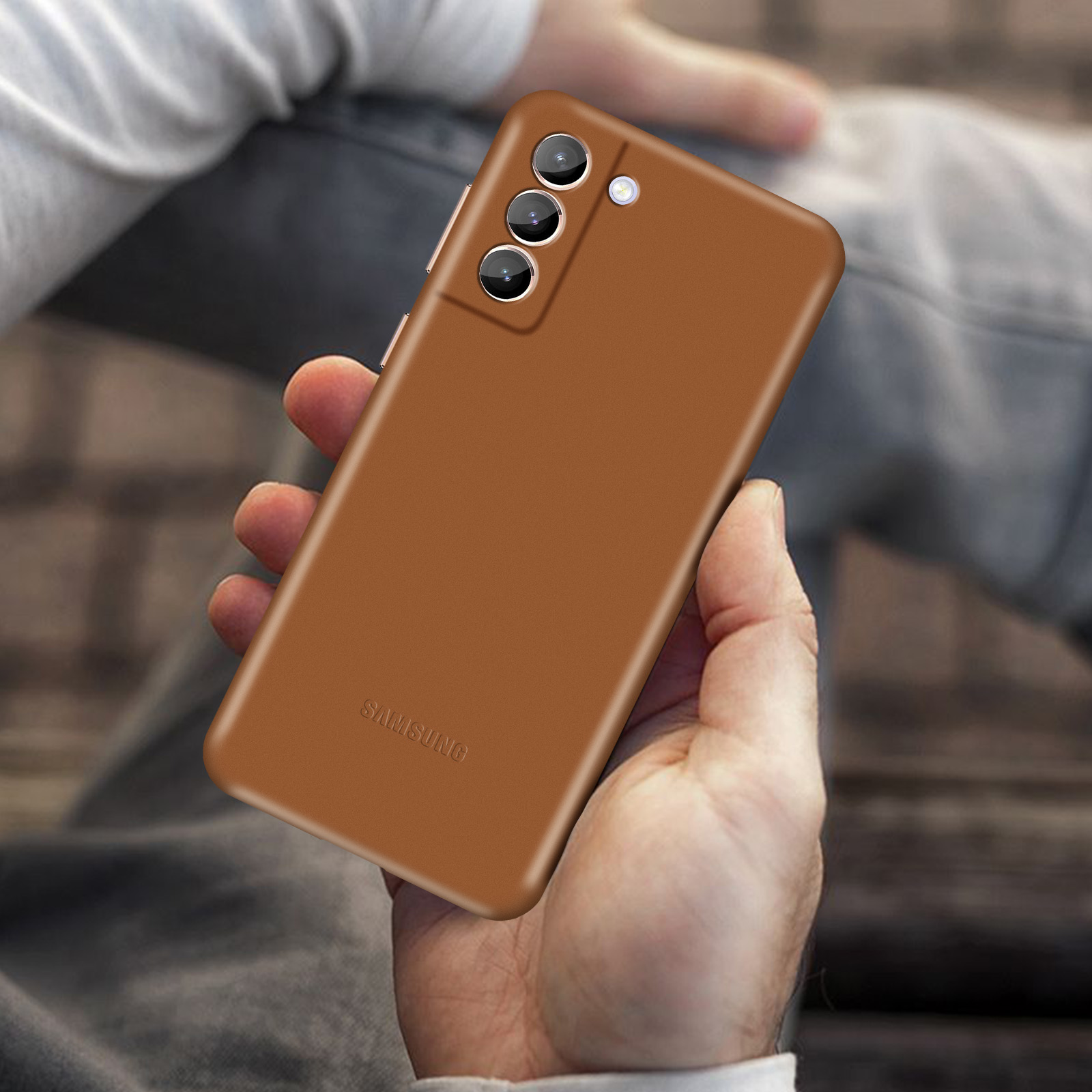 Custodia marrone con tre fotocamere. Logo Samsung. In mano. Sfondo sfocato.