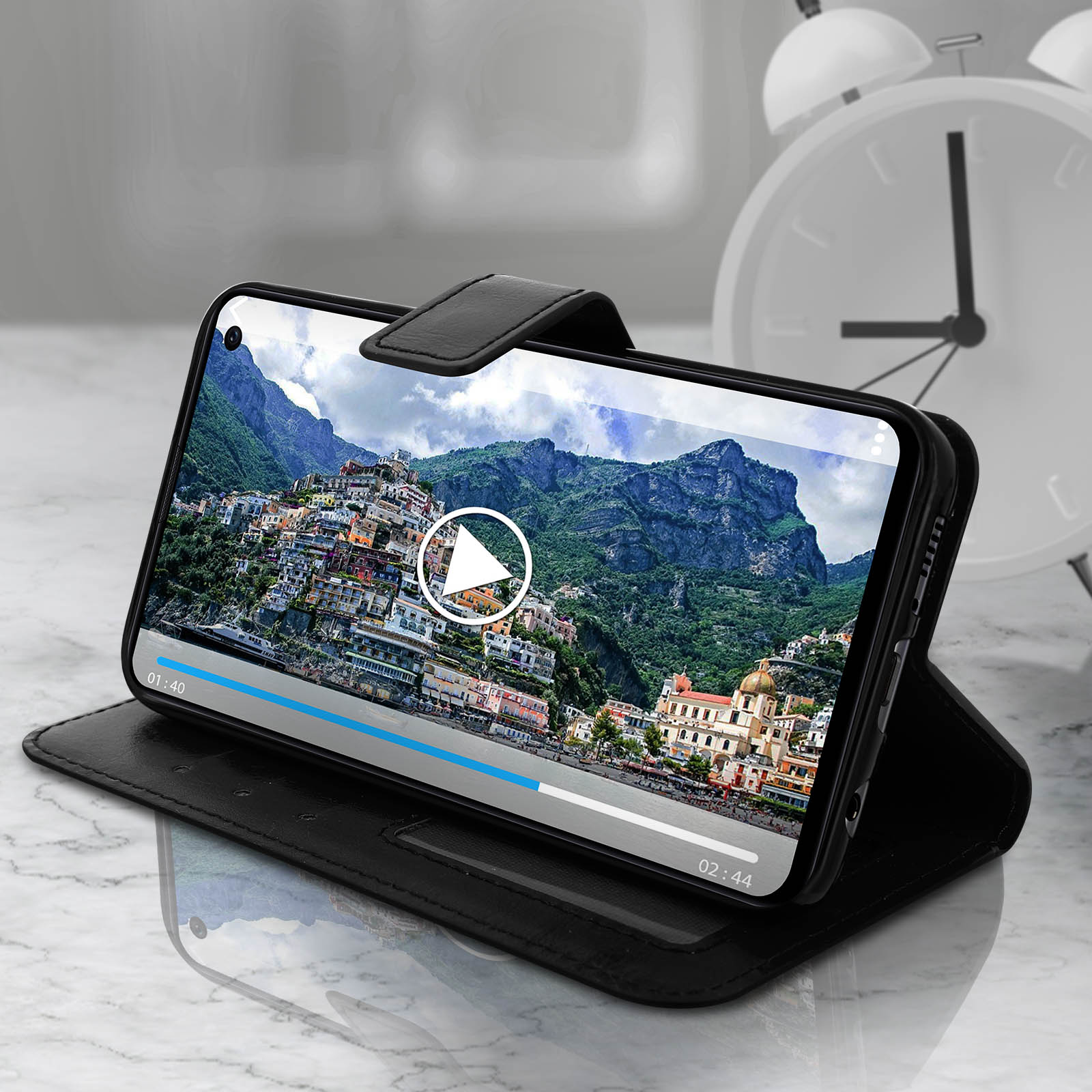 Telefon spielt Video auf Tisch, schwarze Hülle, weißer Wecker.