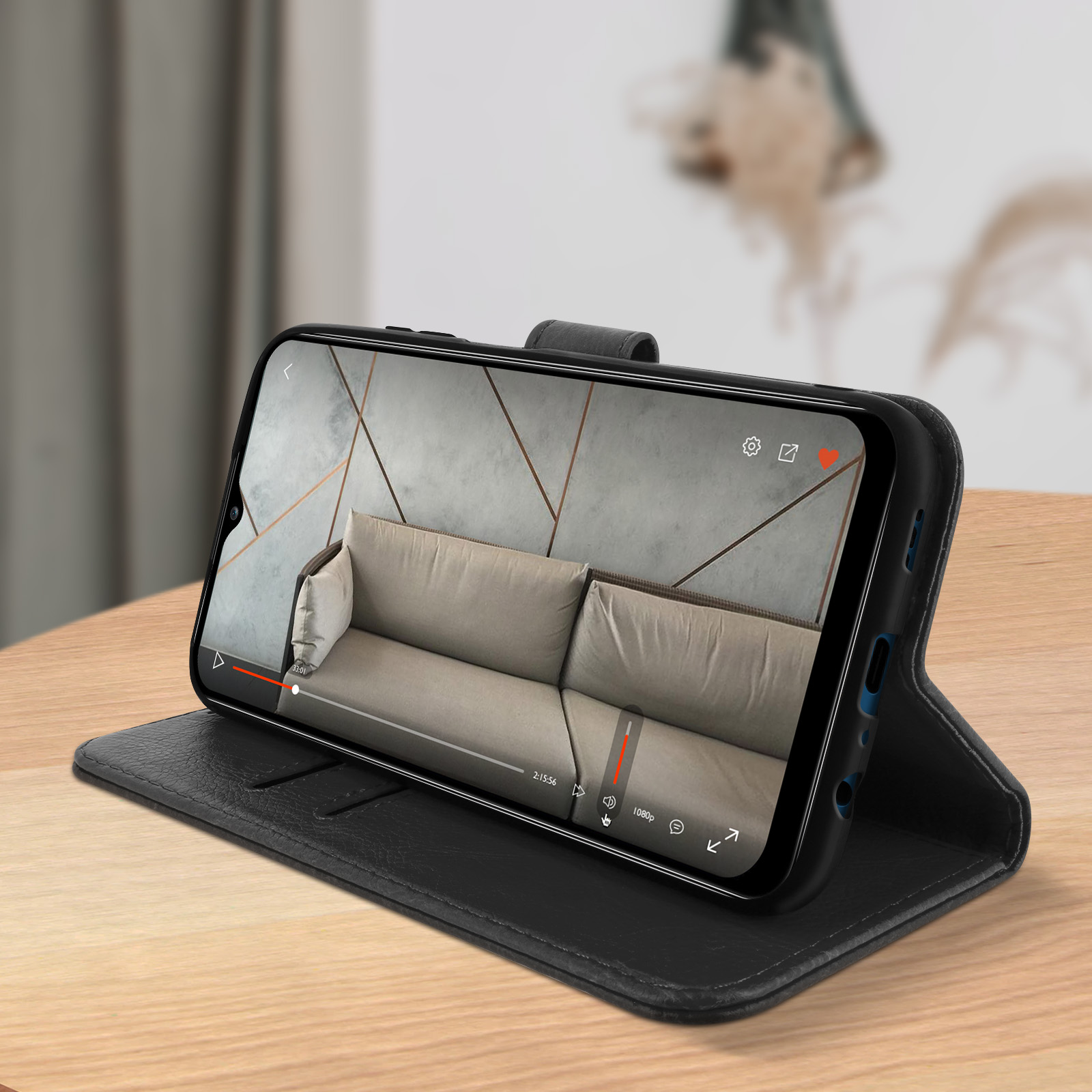 Schwarze Handyhülle mit einem Telefon, das ein Video auf einer Holzoberfläche anzeigt. Ein Sofa ist unscharf.
