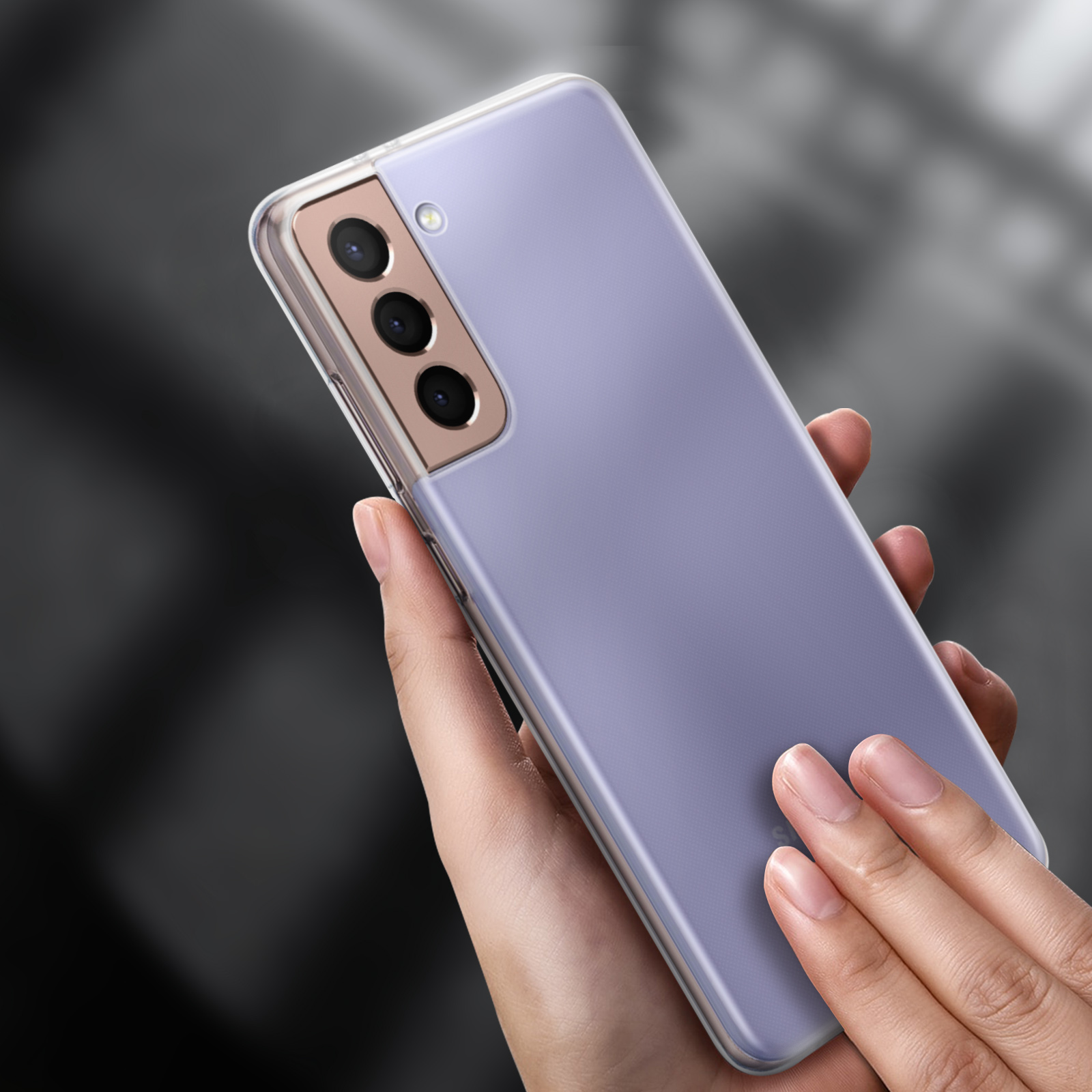 Un étui de téléphone transparent avec une teinte violette est tenu dans les mains. Il possède une triple caméra et est tenu contre un arrière-plan flou.