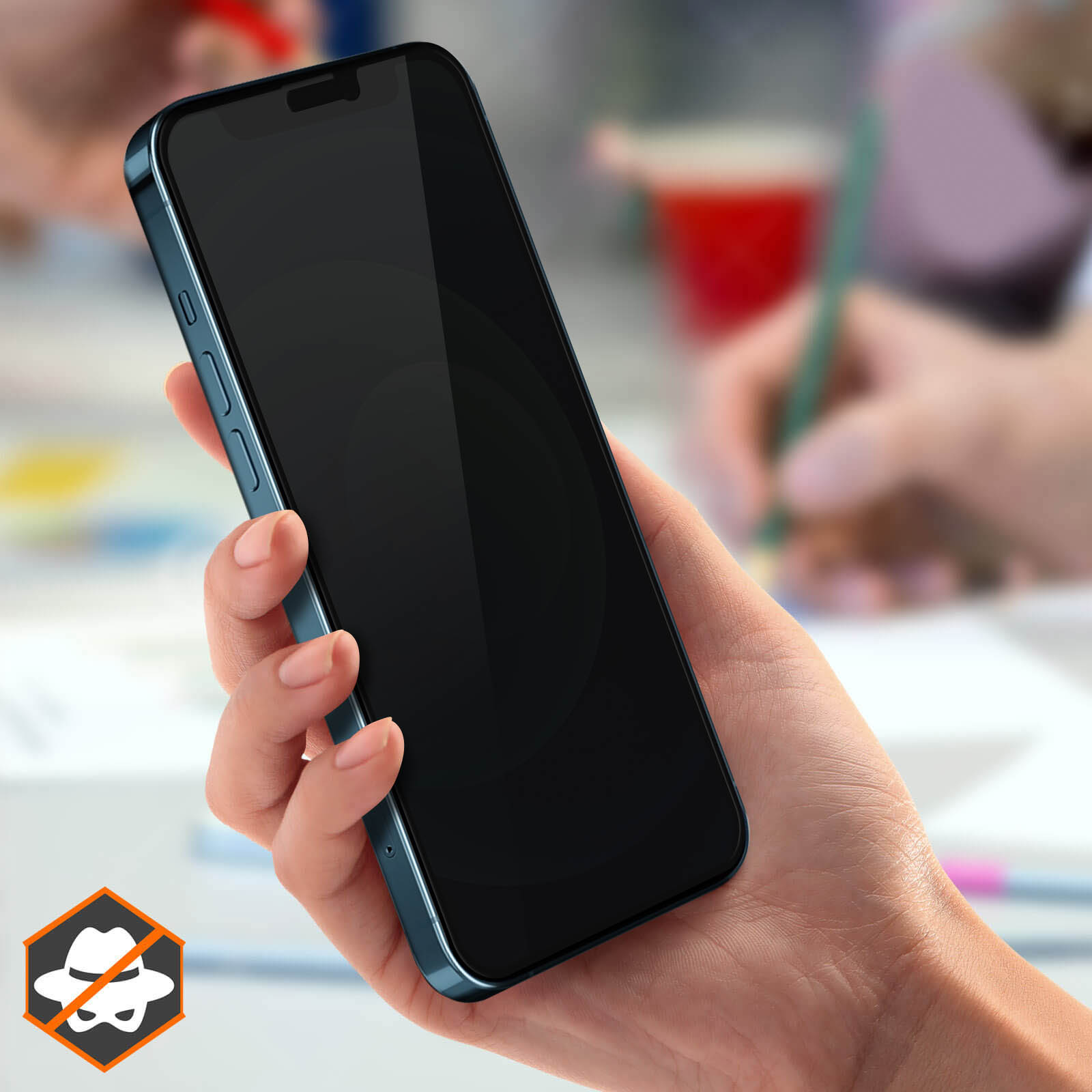 Una mano che tiene uno smartphone nero. Sullo sfondo, altre mani e oggetti sono leggermente sfocati.