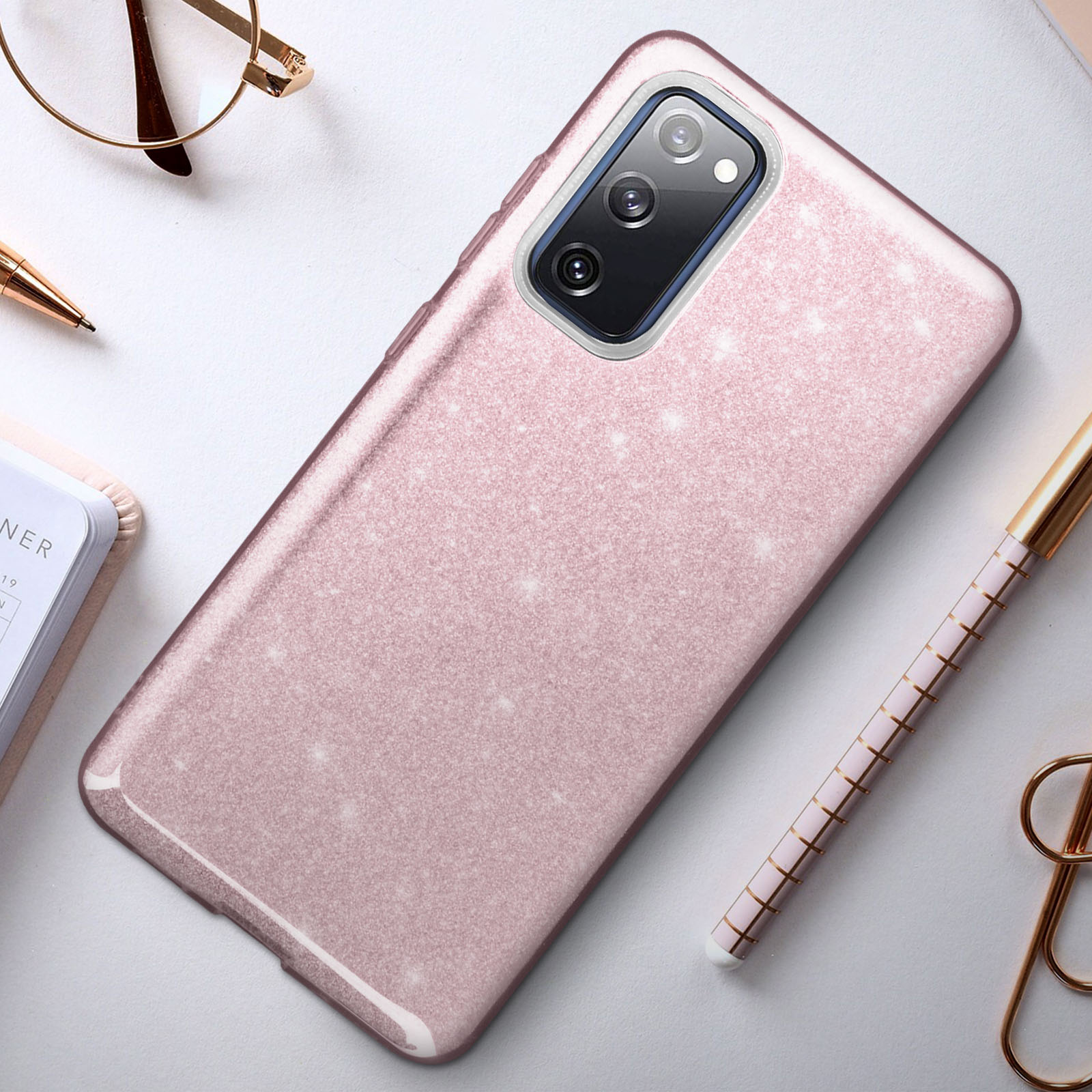 Custodia rosa con glitter, telefono e penna sul tavolo.