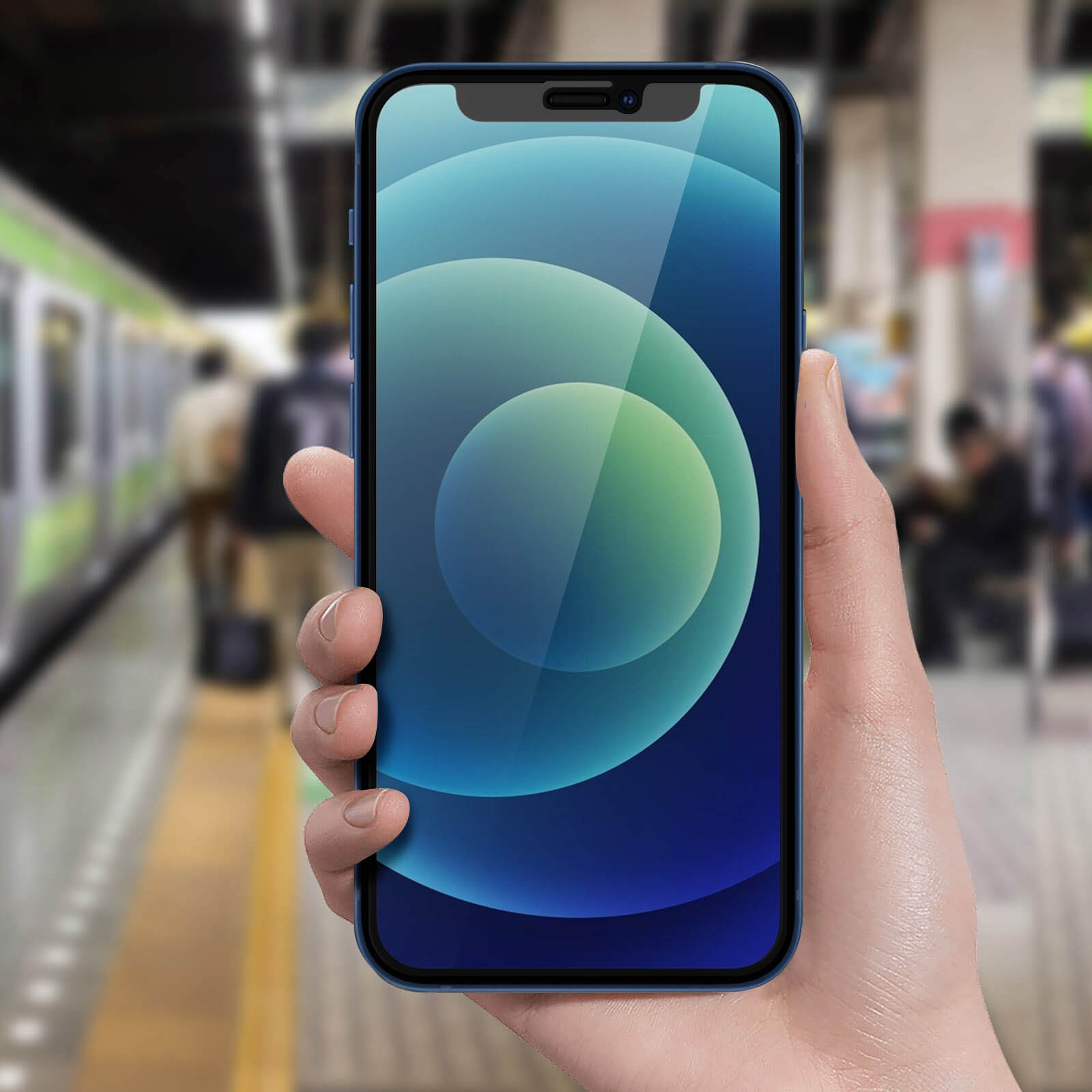 Una mano tiene un iPhone blu con display sfumato blu e verde. Persone e un treno sullo sfondo sfocato.