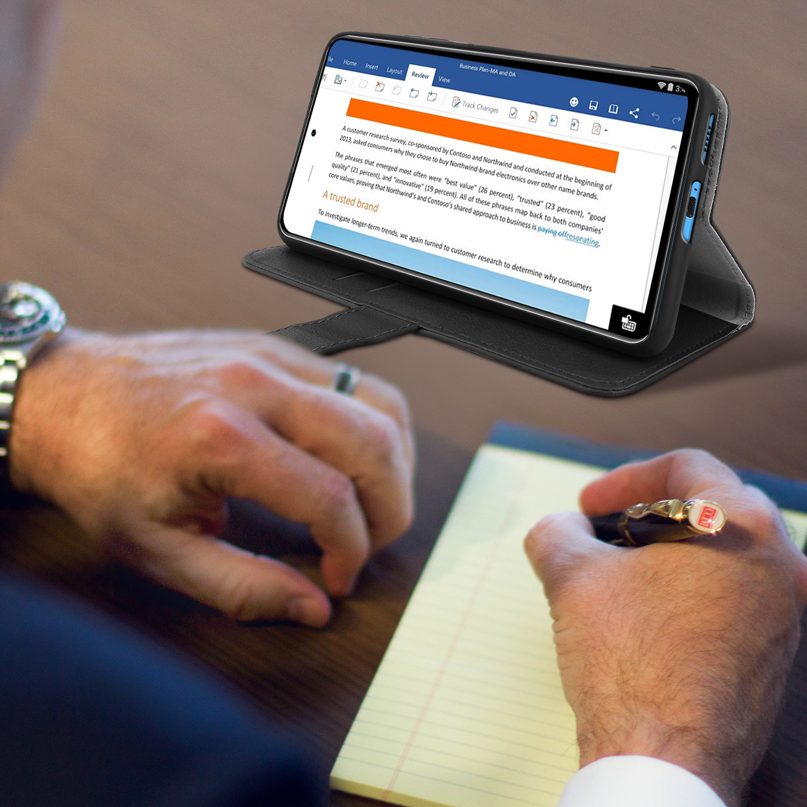 Una persona scrive su un blocco note mentre guarda un telefono con un documento. Il telefono è in una custodia.