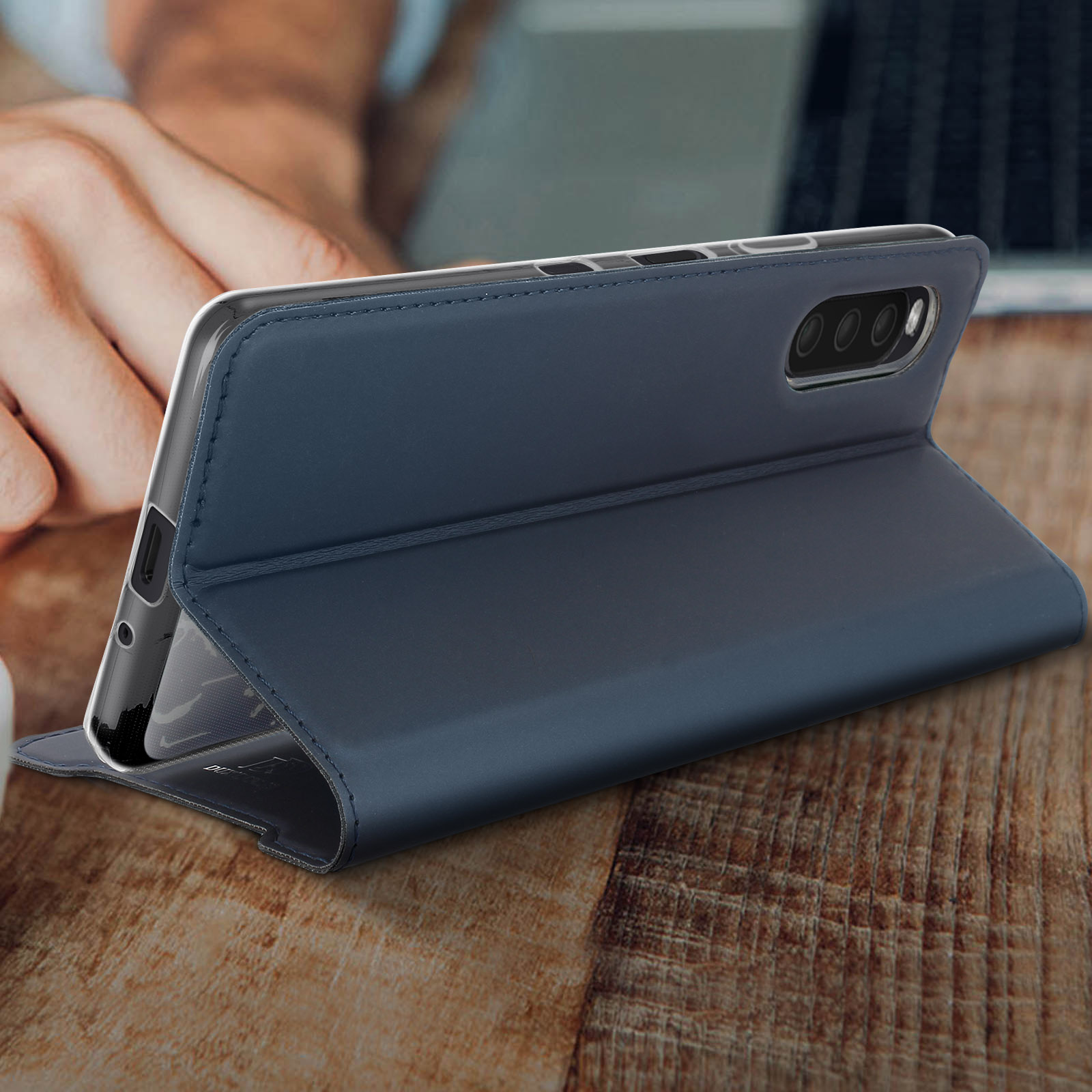 Una custodia blu per telefono è aperta, rivelando il telefono. Una mano è sfocata sullo sfondo.