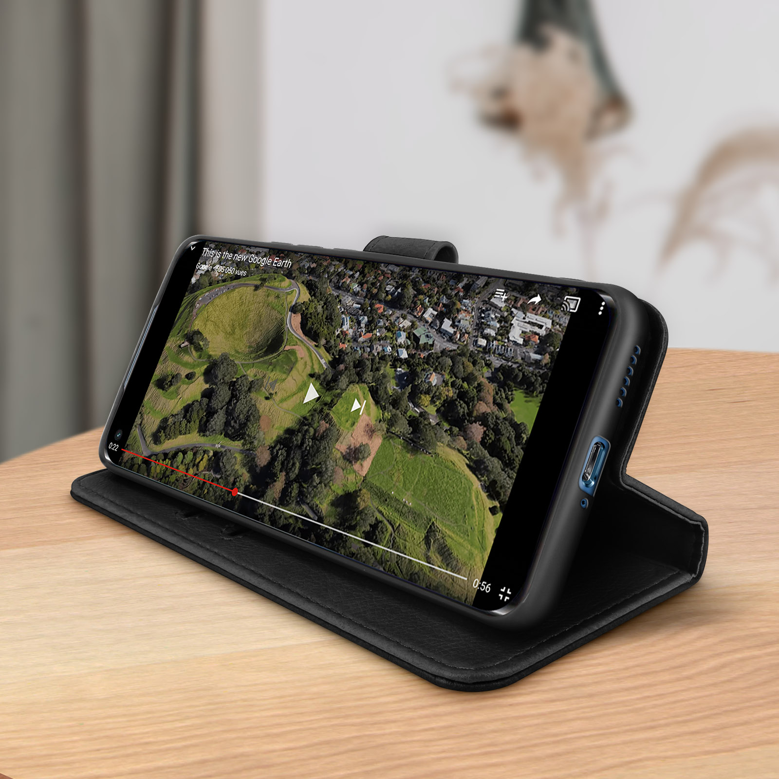 Een telefoon in een zwart hoesje met een video van een groen landschap. Op een houten tafel.