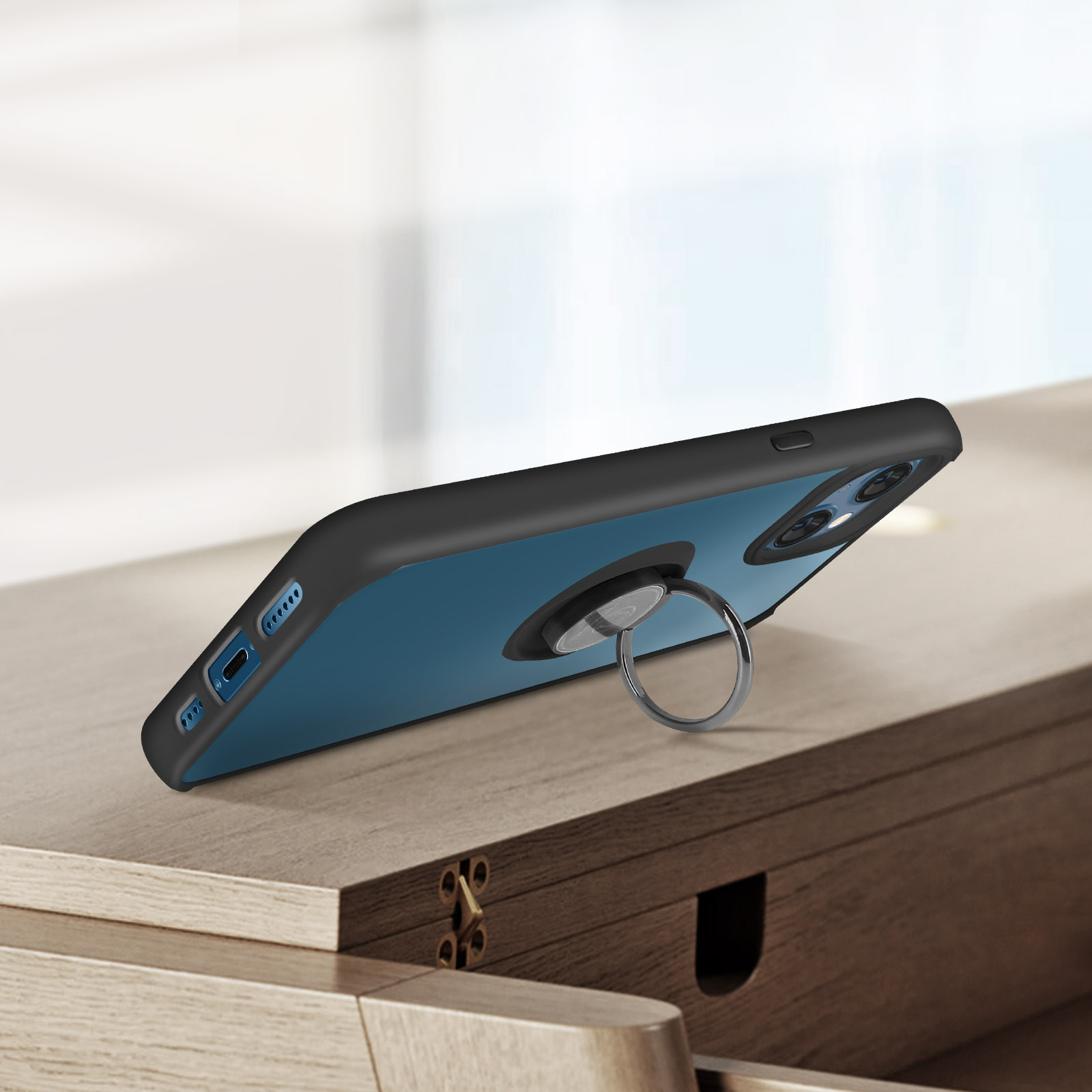 Un téléphone noir dans un étui avec un support d'anneau argenté. Le fond est une table en bois.