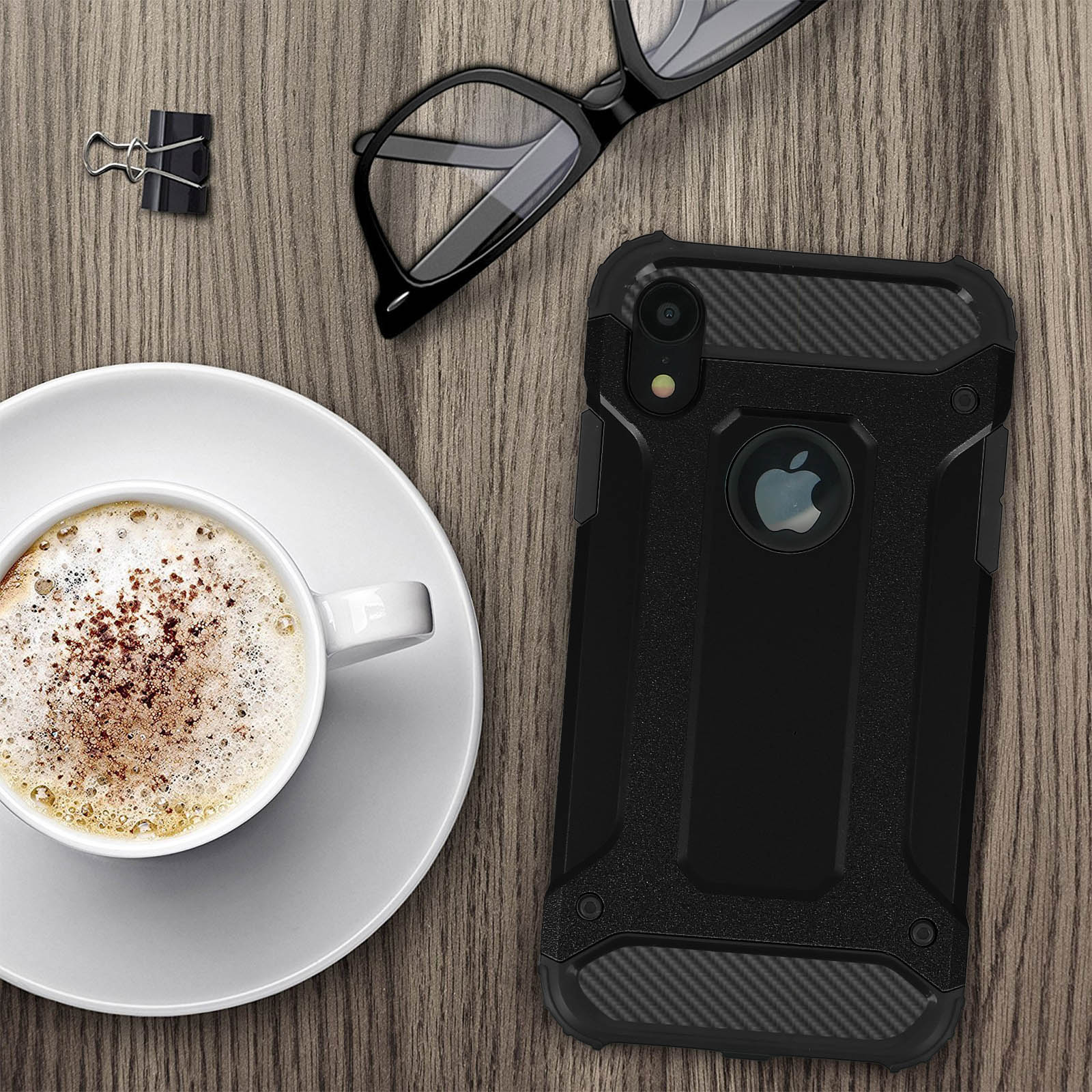 Una custodia per telefono accanto a caffè, occhiali e una graffetta. L'ambientazione è un tavolo di legno.