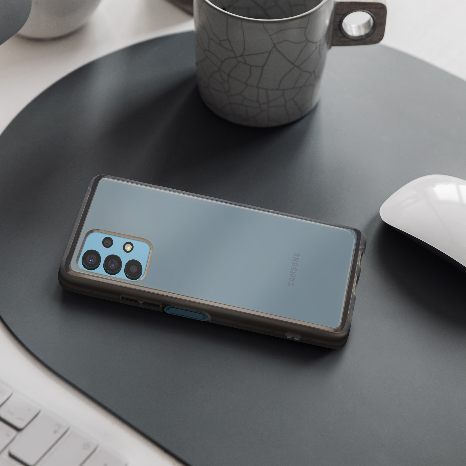 Teléfono con funda en alfombra negra. Taza y ratón en escritorio. Funda Samsung a la vista.