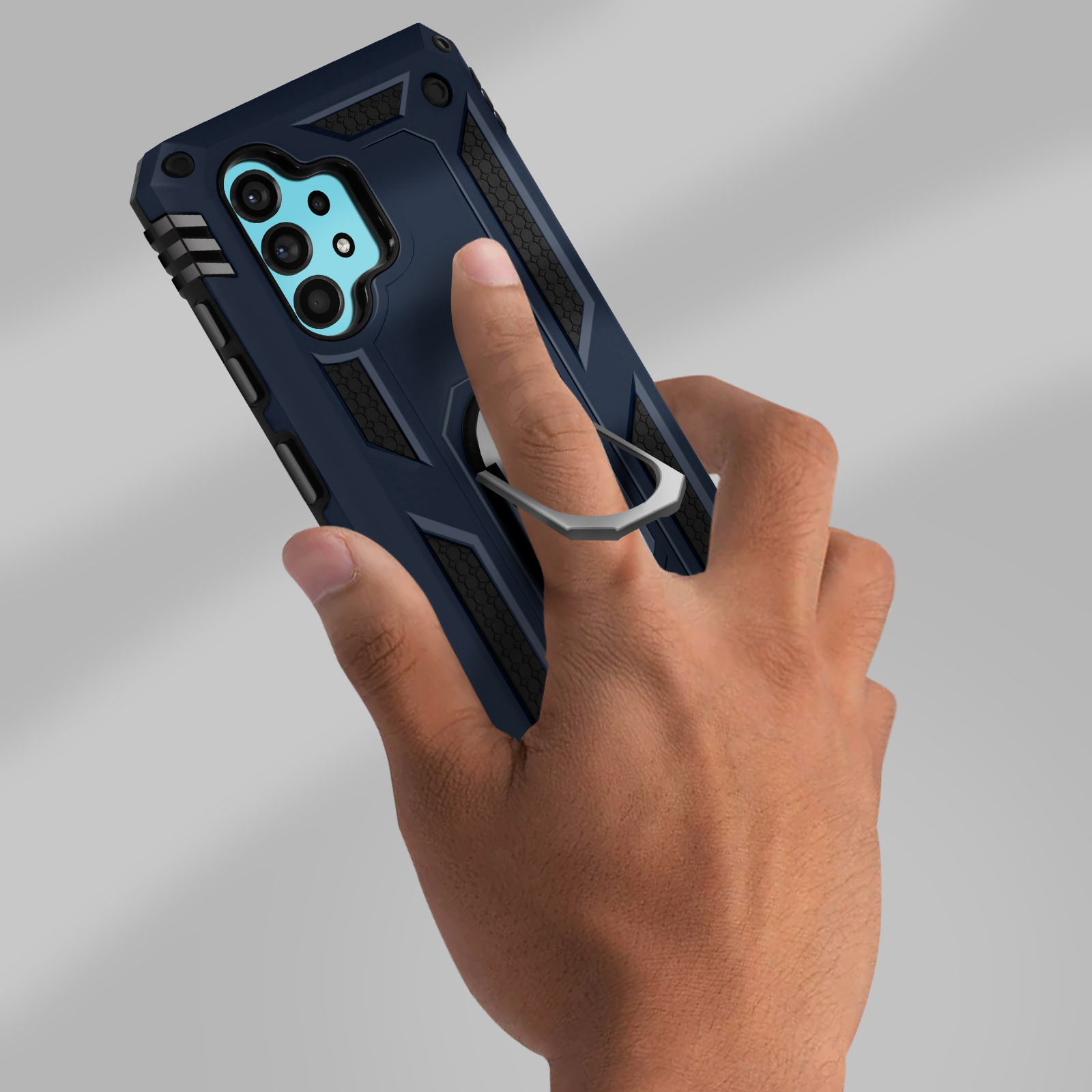 Una mano che tiene una custodia blu e nera per telefono con un anello, su sfondo grigio chiaro.