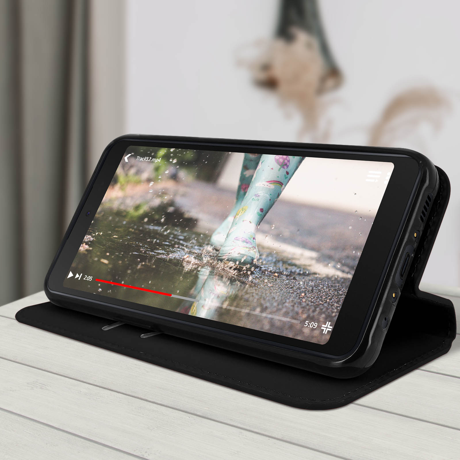 Téléphone affichant une vidéo de pieds dans l'eau, dans un étui noir sur une table.