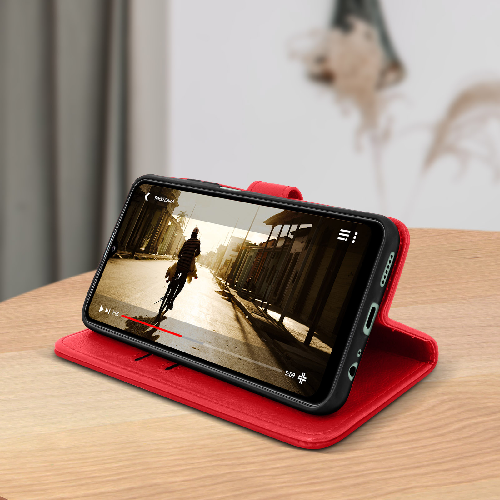 Un téléphone avec une coque rouge affiche une vidéo sur une table en bois. La scène est à l'intérieur.