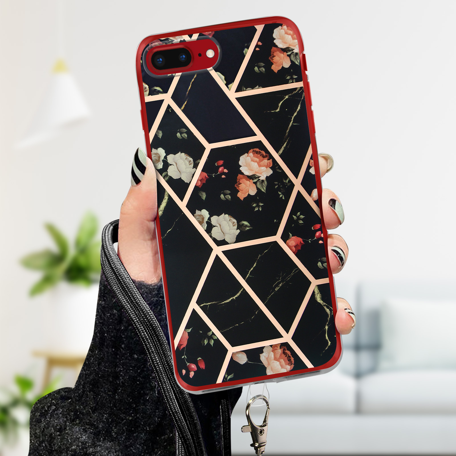 Mano che tiene telefono in custodia nera con design floreale. Bordo dorato. Sfondo sfocato.