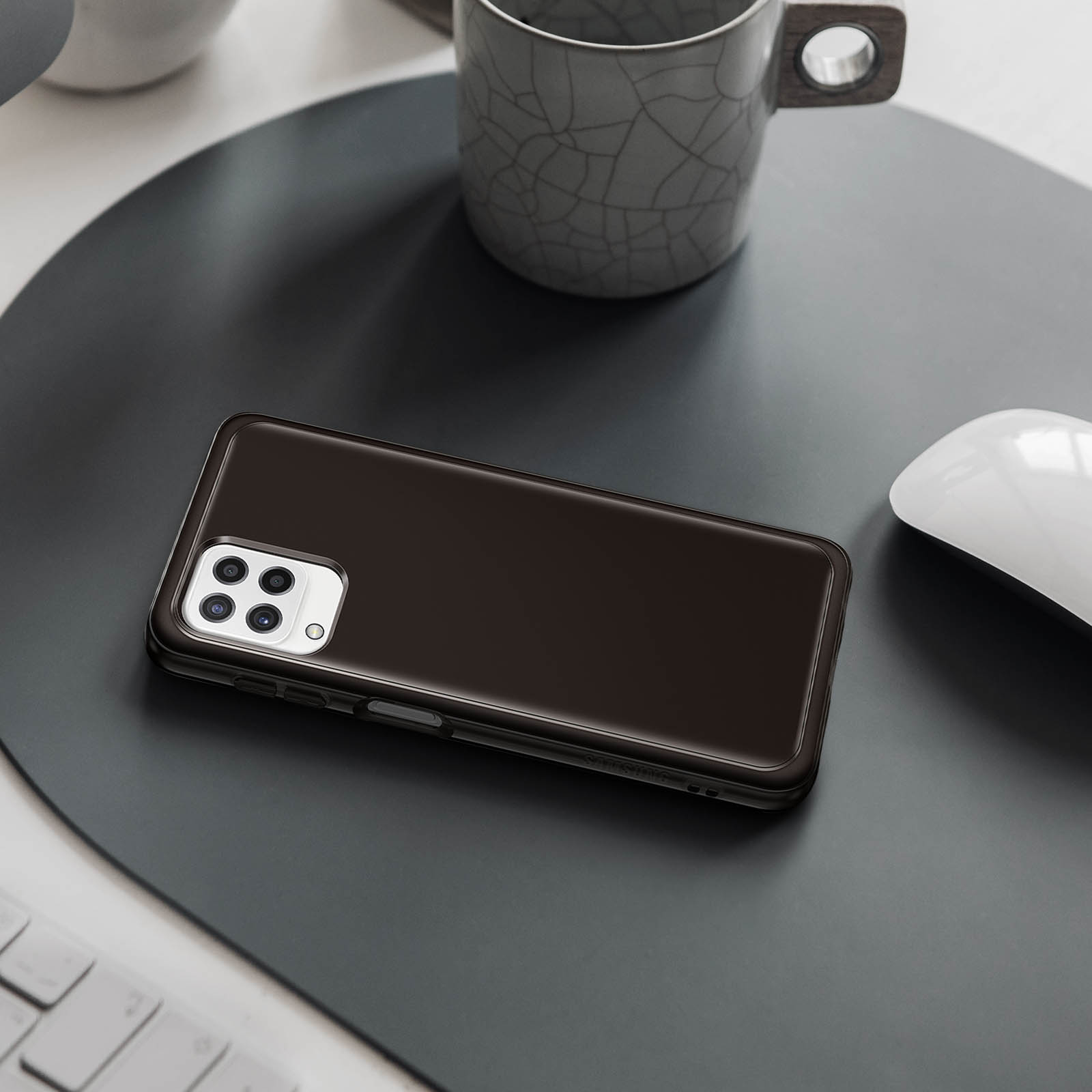 Czarny telefon na ciemnoszarej powierzchni. Widoczny kubek i mysz. Widok z góry.