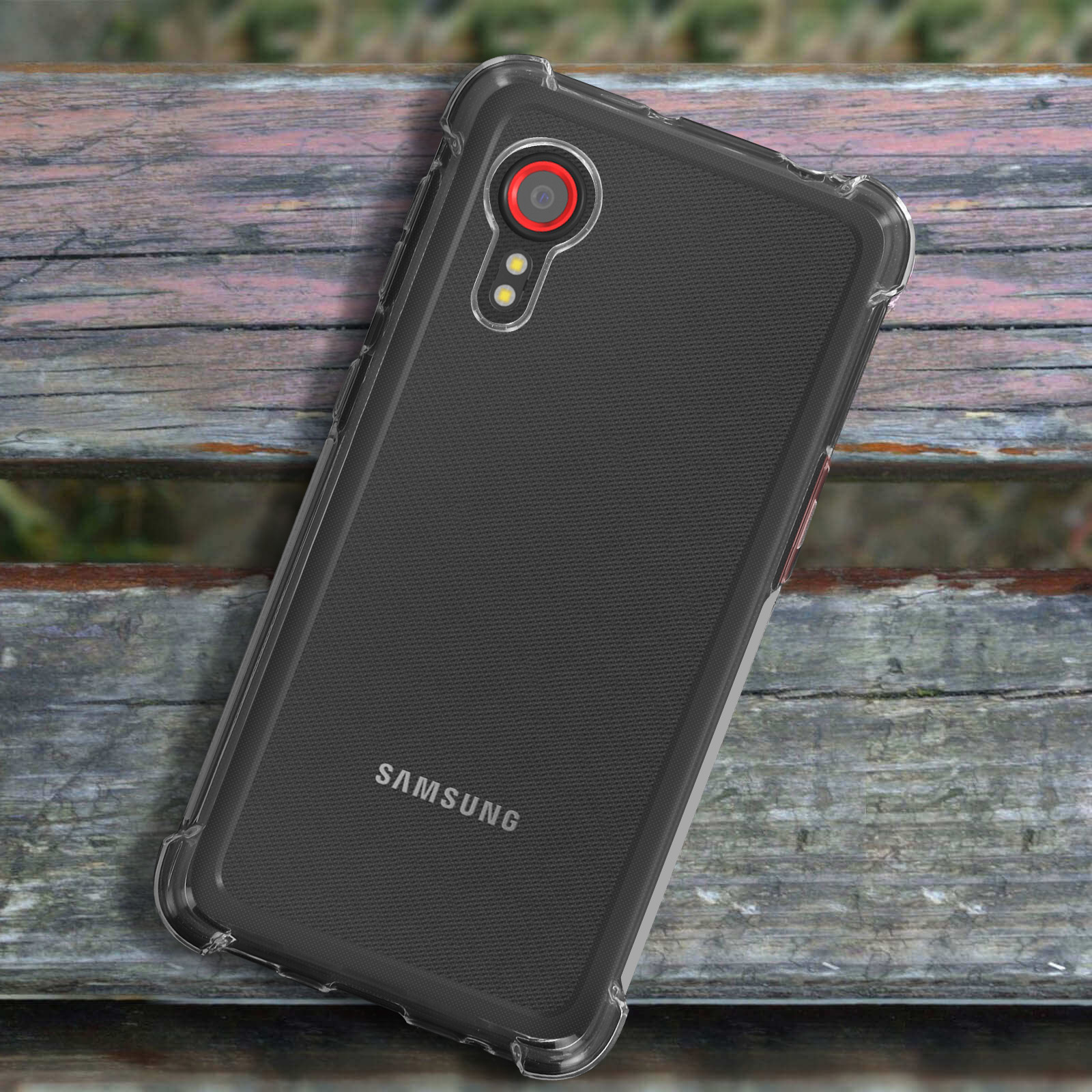 Un telefono nero in una custodia trasparente su una panchina di legno. La custodia ha angoli rinforzati, logo Samsung.