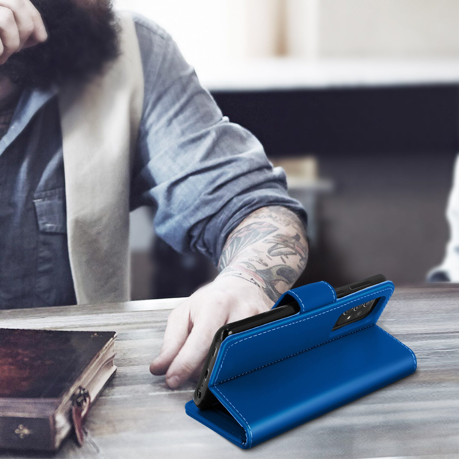 Una custodia blu per telefono è aperta su un tavolo, con un uomo sullo sfondo.
