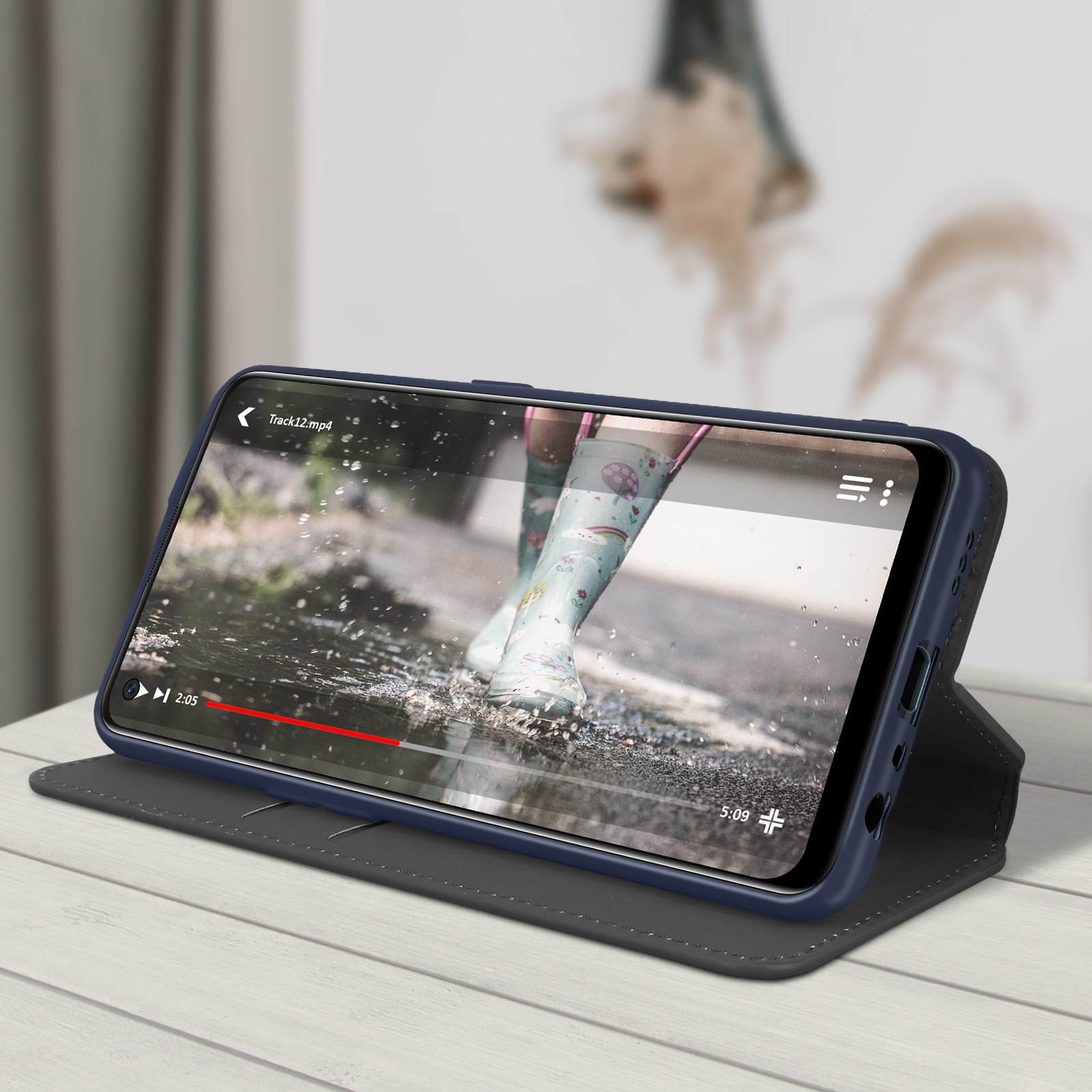 Il telefono in una custodia blu scuro mostra un video di stivali nell'acqua. La custodia è su un tavolo.