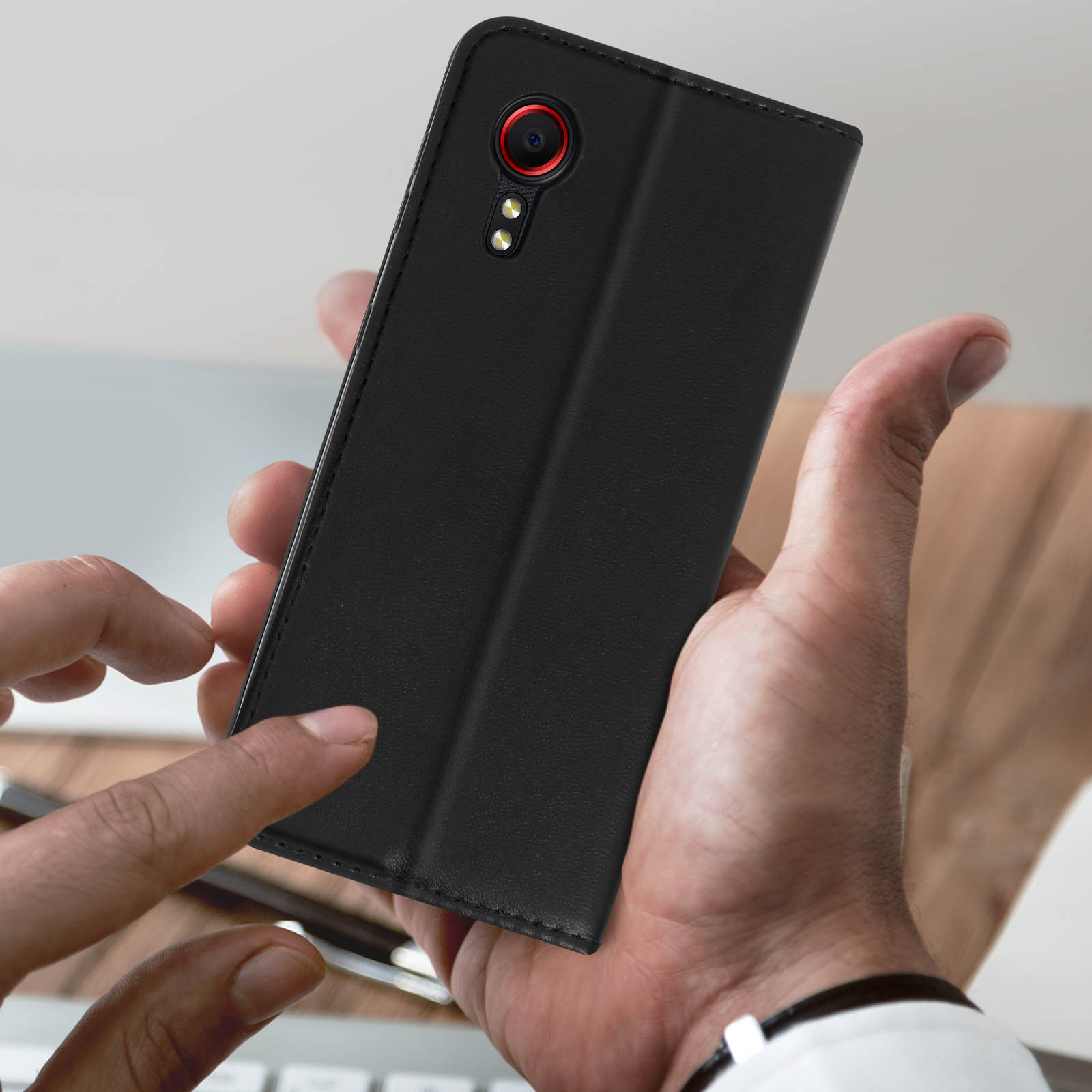 Una custodia in pelle nera, aperta, con un telefono dentro. Una mano indica il telefono.