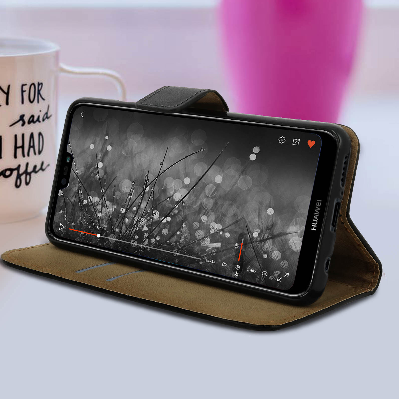 Telefono in una custodia, che mostra un video con dettagli d'erba, su un tavolo. Tazza e forma rosa sullo sfondo.
