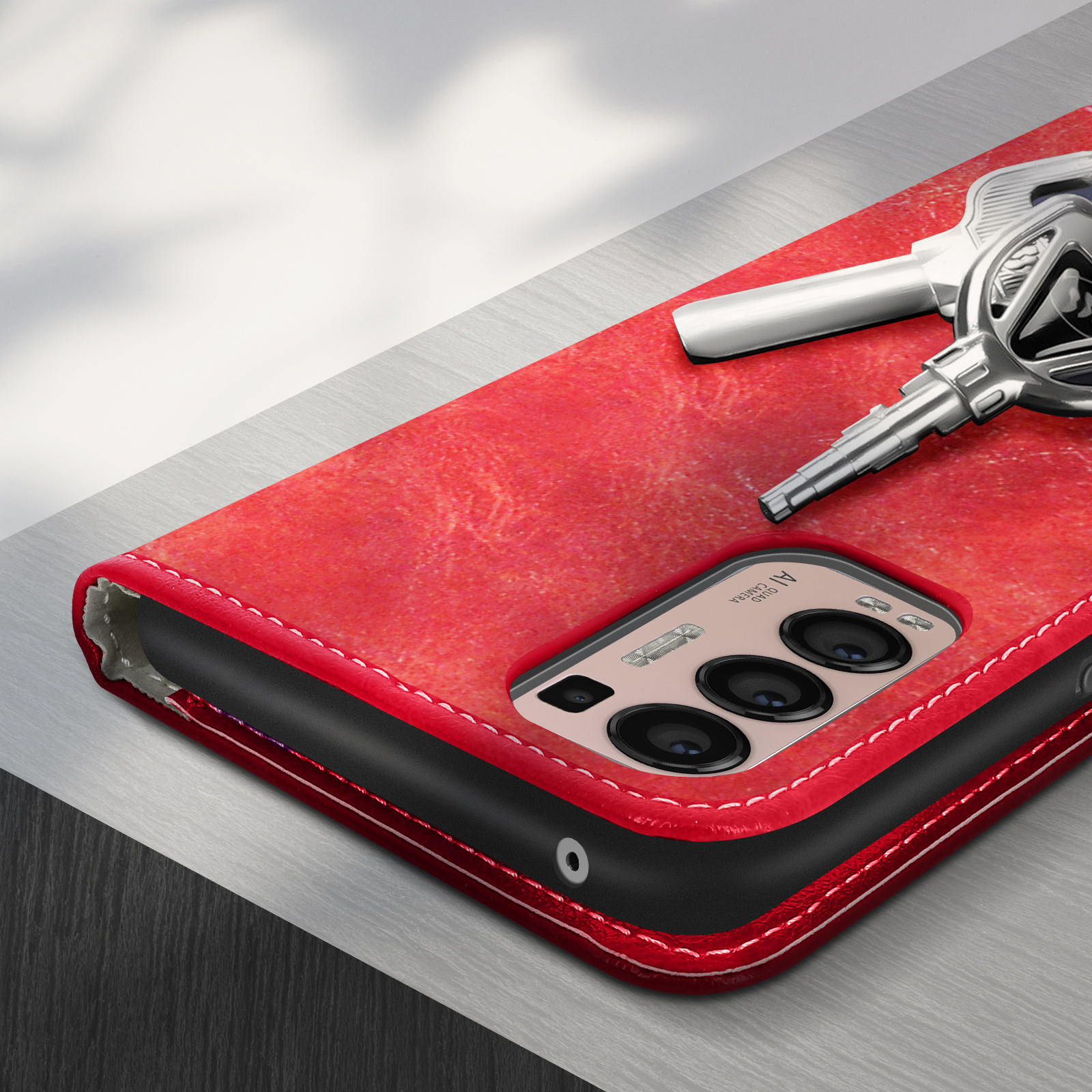 Une coque de téléphone rouge avec des clés sur une surface métallique. Le téléphone a plusieurs caméras.