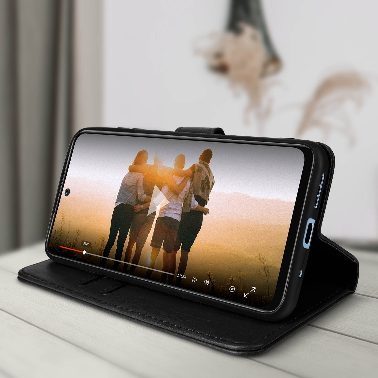 Zwarte telefoonhoes met een telefoon met een video van mensen is open op een tafel.