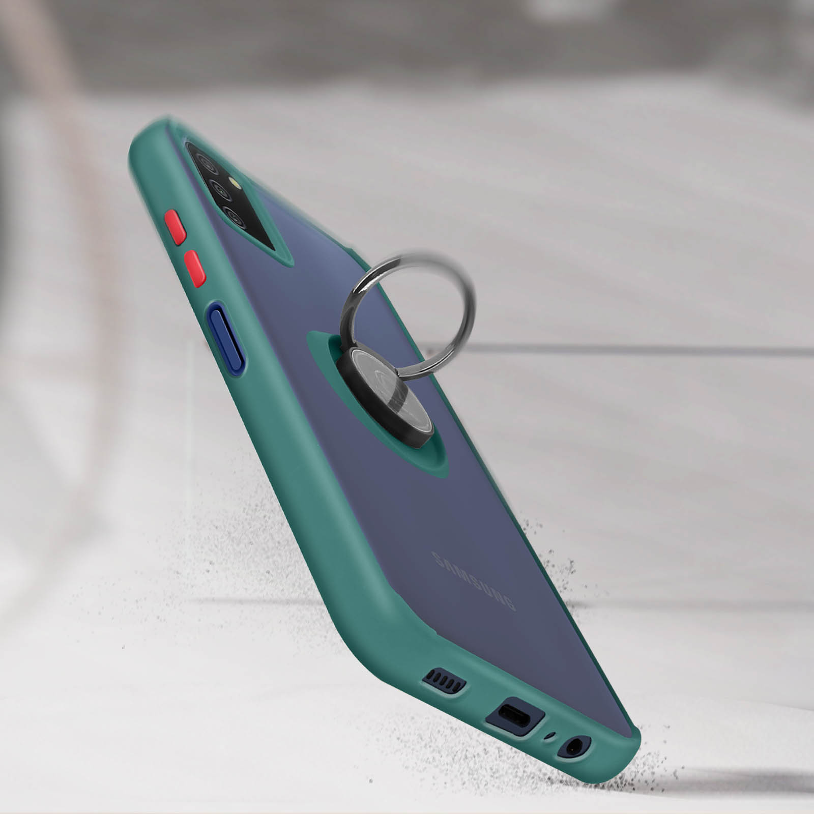 Una custodia per telefono verde acqua con supporto ad anello sta cadendo. Lo sfondo è sfocato con un tono grigio chiaro.