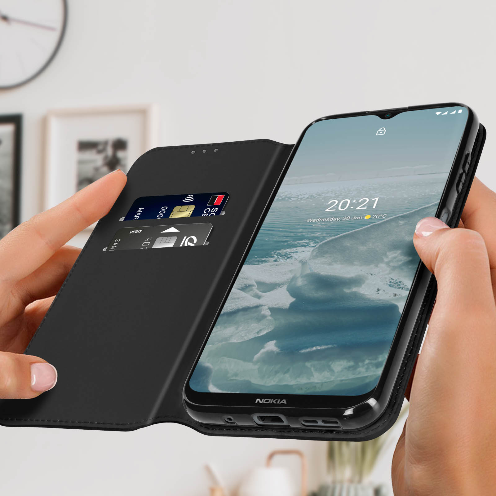 Custodia nera con carte di credito, telefono aperto. Sfondo: muro sfocato, immagine incorniciata.