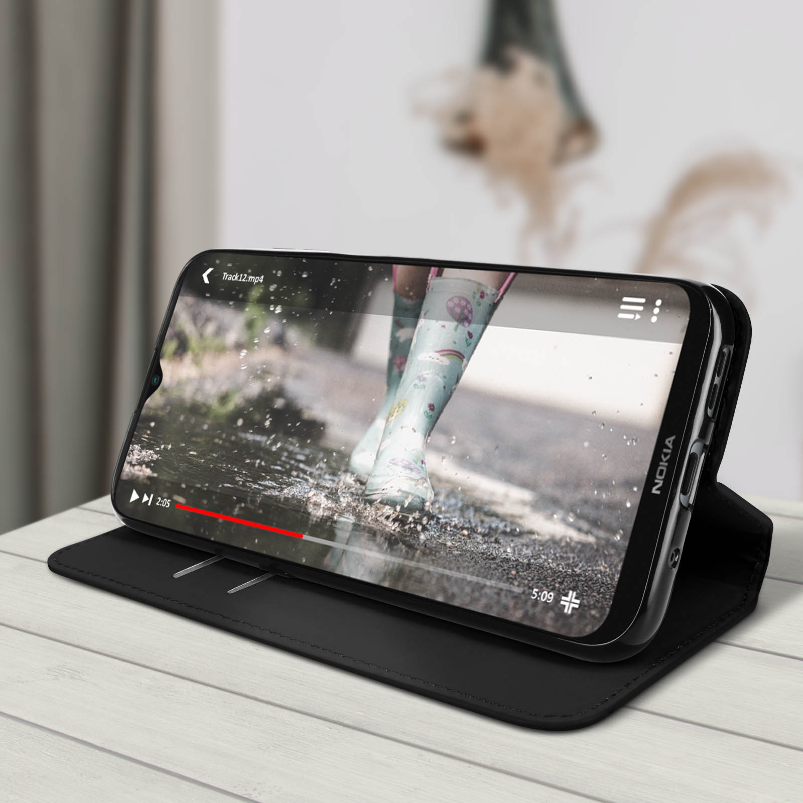 Il telefono mostra video di stivali in pozzanghera. Custodia nera su legno.