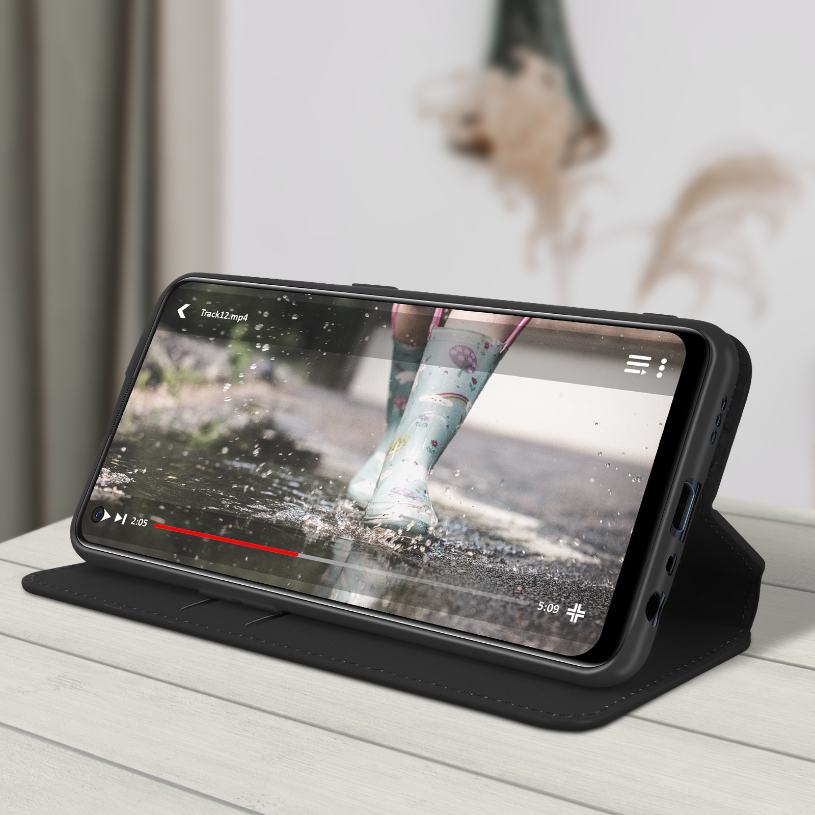 Téléphone dans un étui noir, montrant une vidéo de bottes dans l'eau. Sur une table en bois.