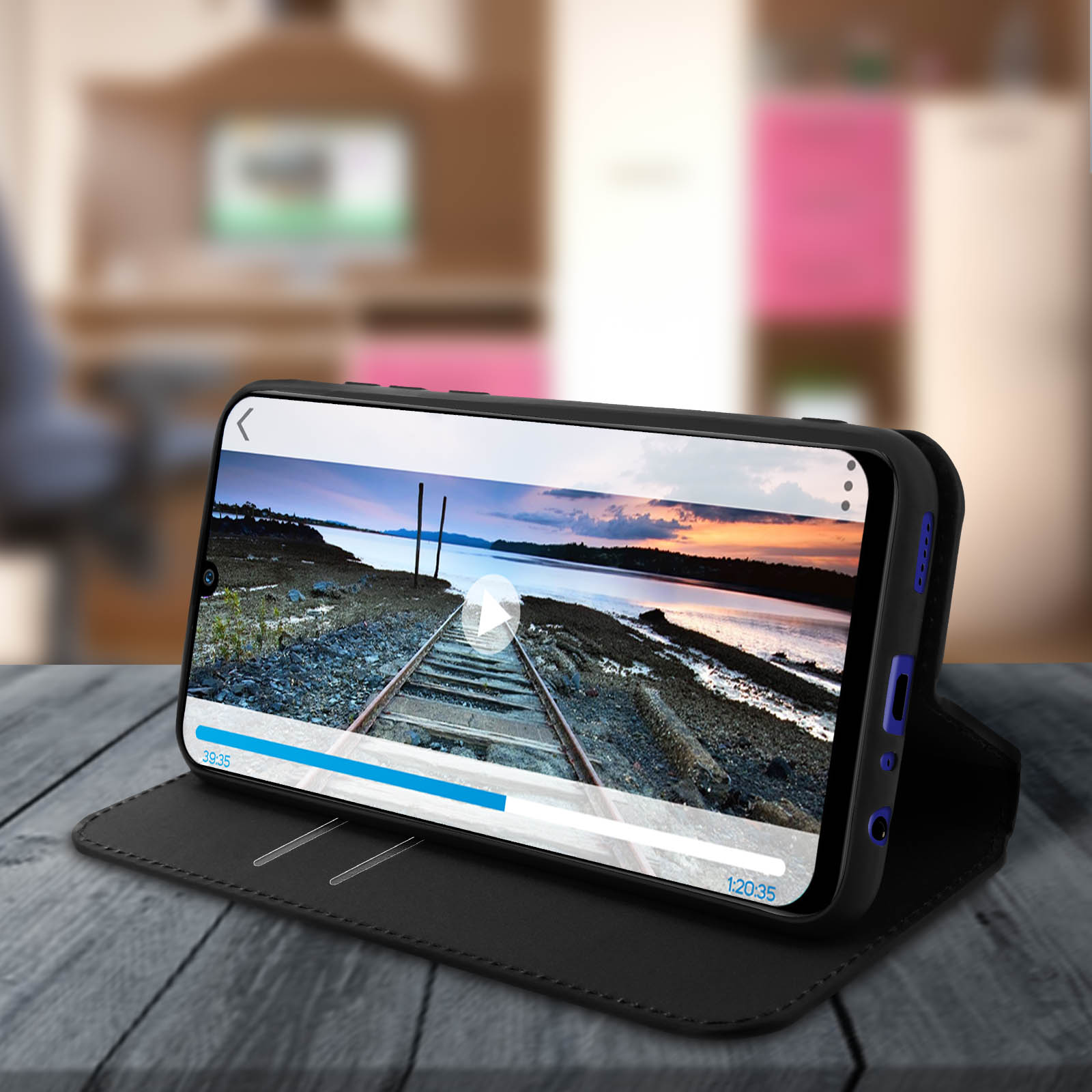 Un telefono nero in una custodia mostra un video. La custodia è aperta su una superficie di legno.