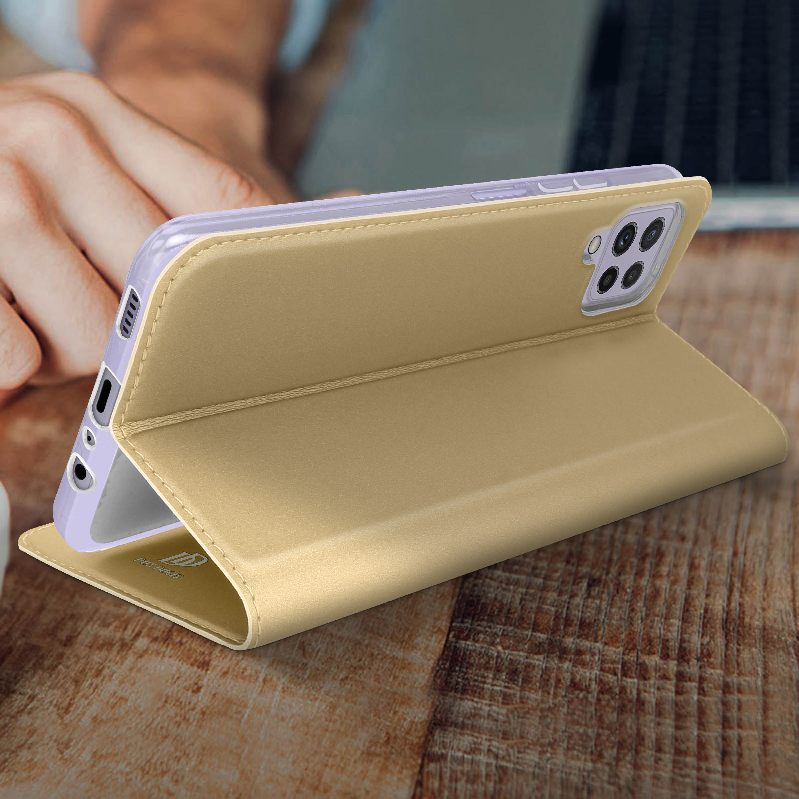 Una funda dorada para teléfono abierta, con un teléfono dentro, colocada sobre una superficie de madera. Una mano es visible.