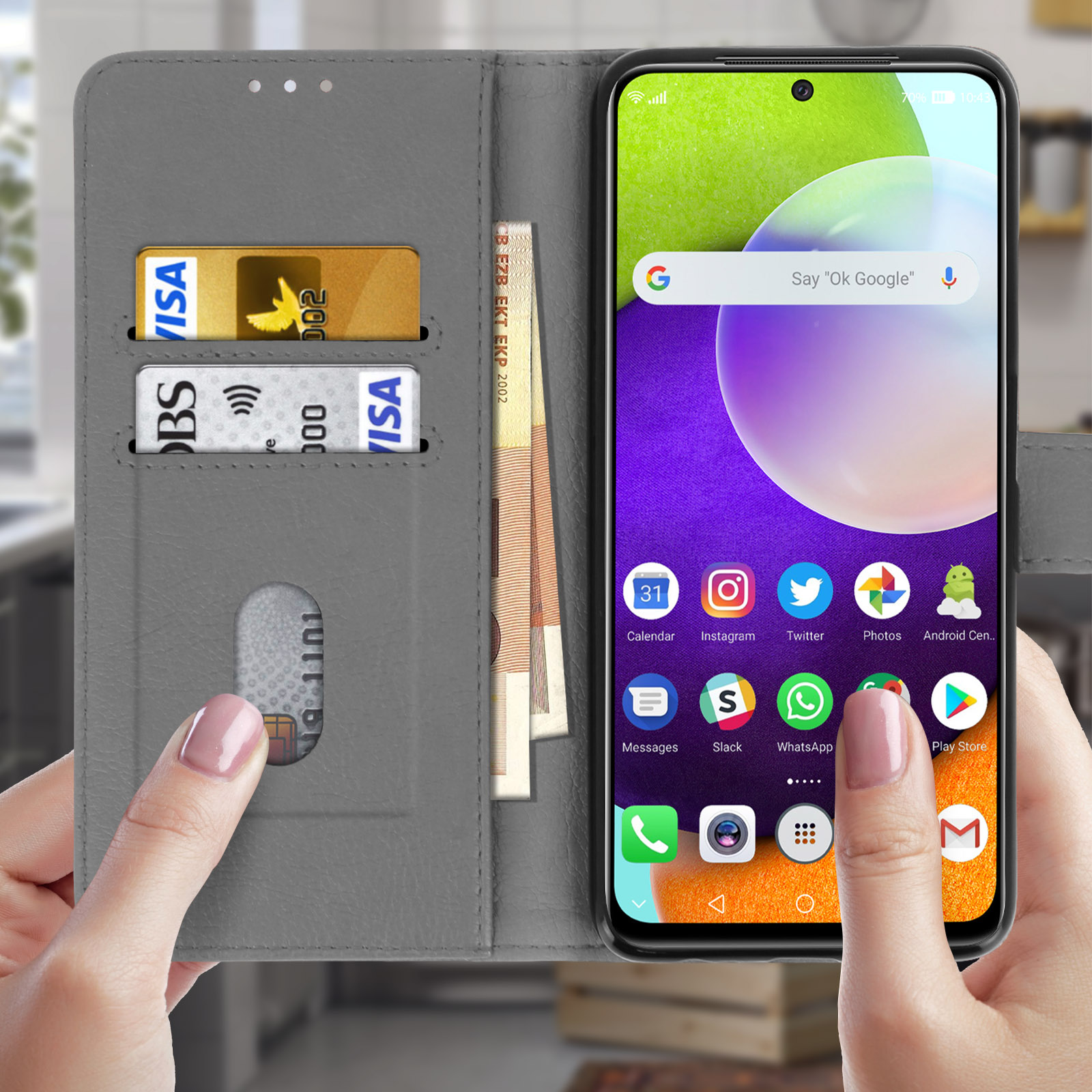 Main tenant un téléphone dans un étui gris, cartes de crédit et argent visibles, avec des icônes à l'écran.