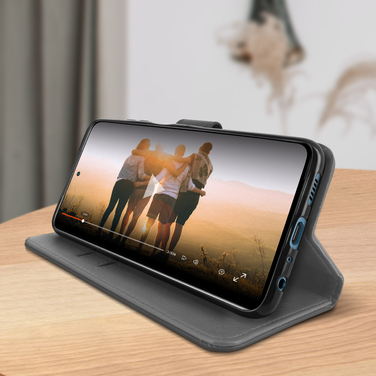 Un téléphone dans un étui gris lit une vidéo. Il est ouvert, montrant une vidéo de personnes.