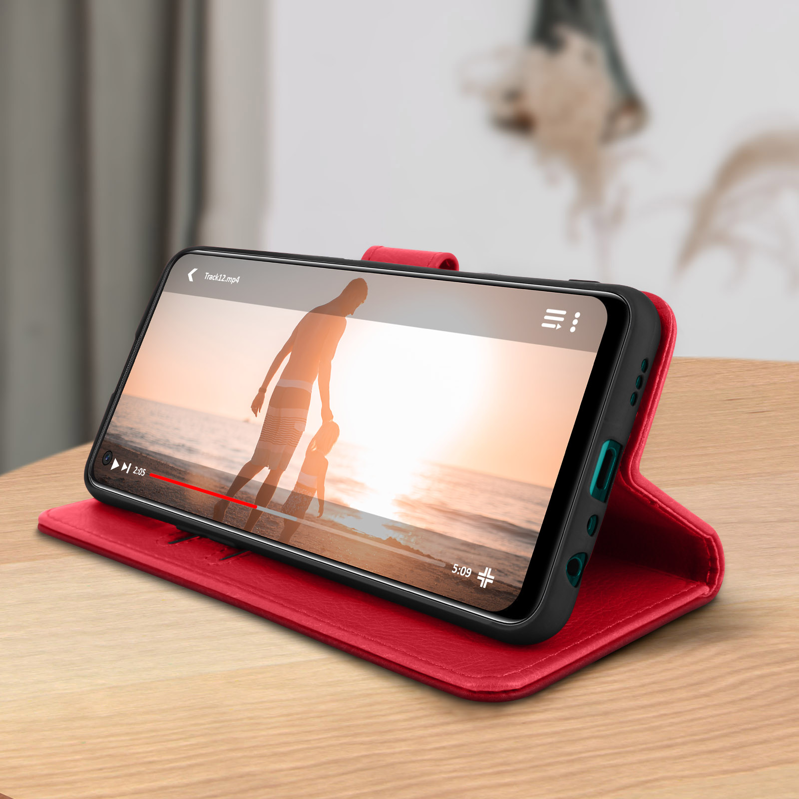Téléphone affichant une vidéo sur un étui rouge. Table en bois.