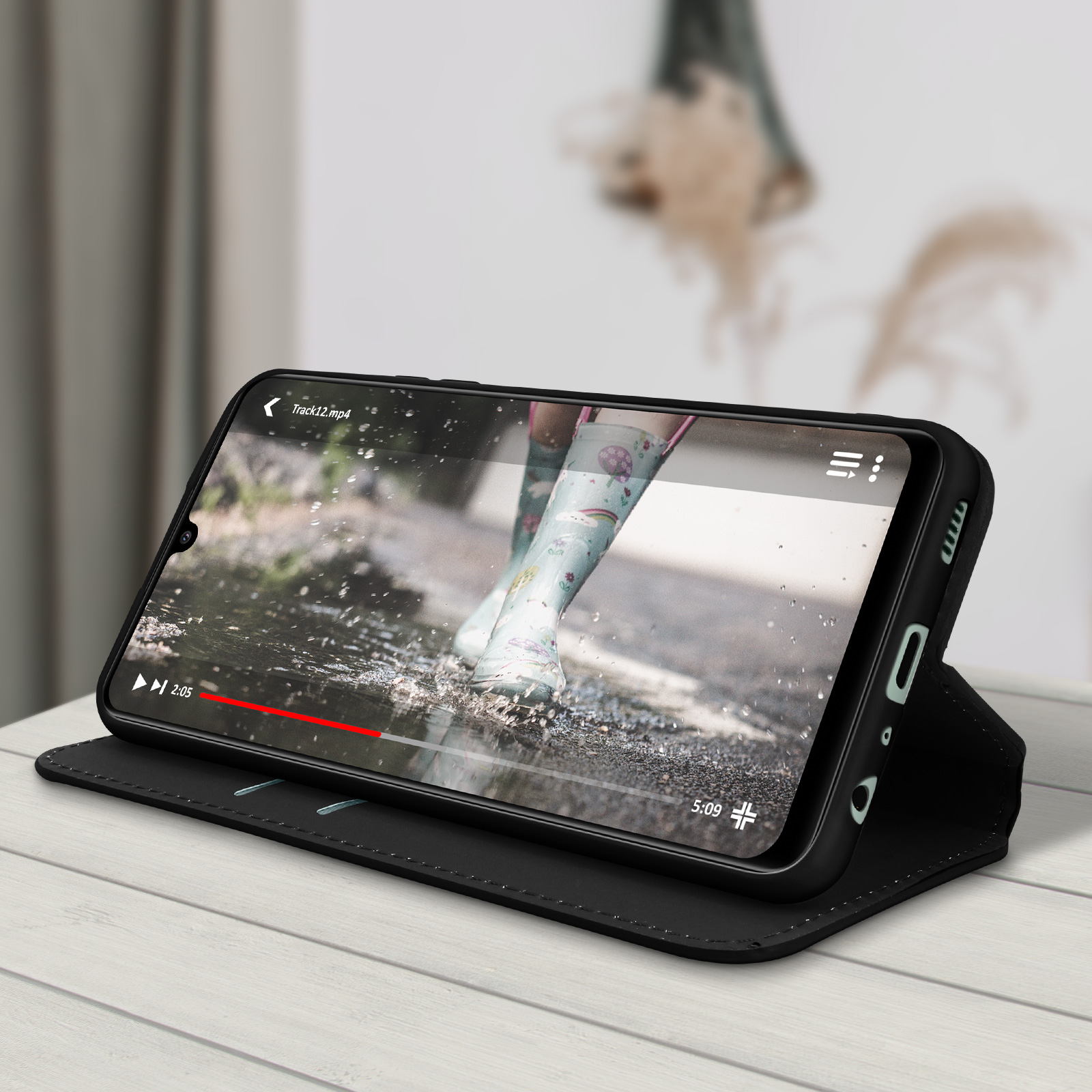 Étui de téléphone noir avec un téléphone diffusant une vidéo. Table en bois et fond neutre.
