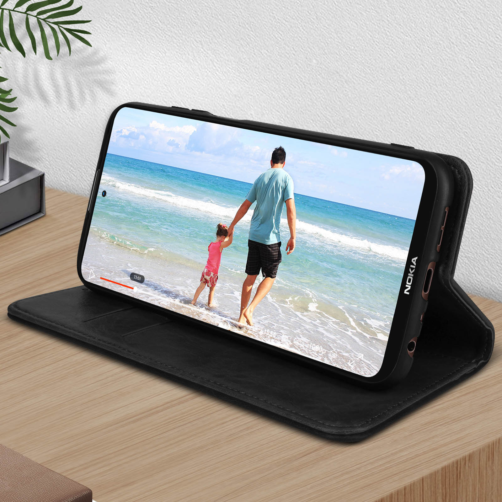 Il telefono mostra un video di un uomo e un bambino sulla spiaggia. Custodia nera su legno.