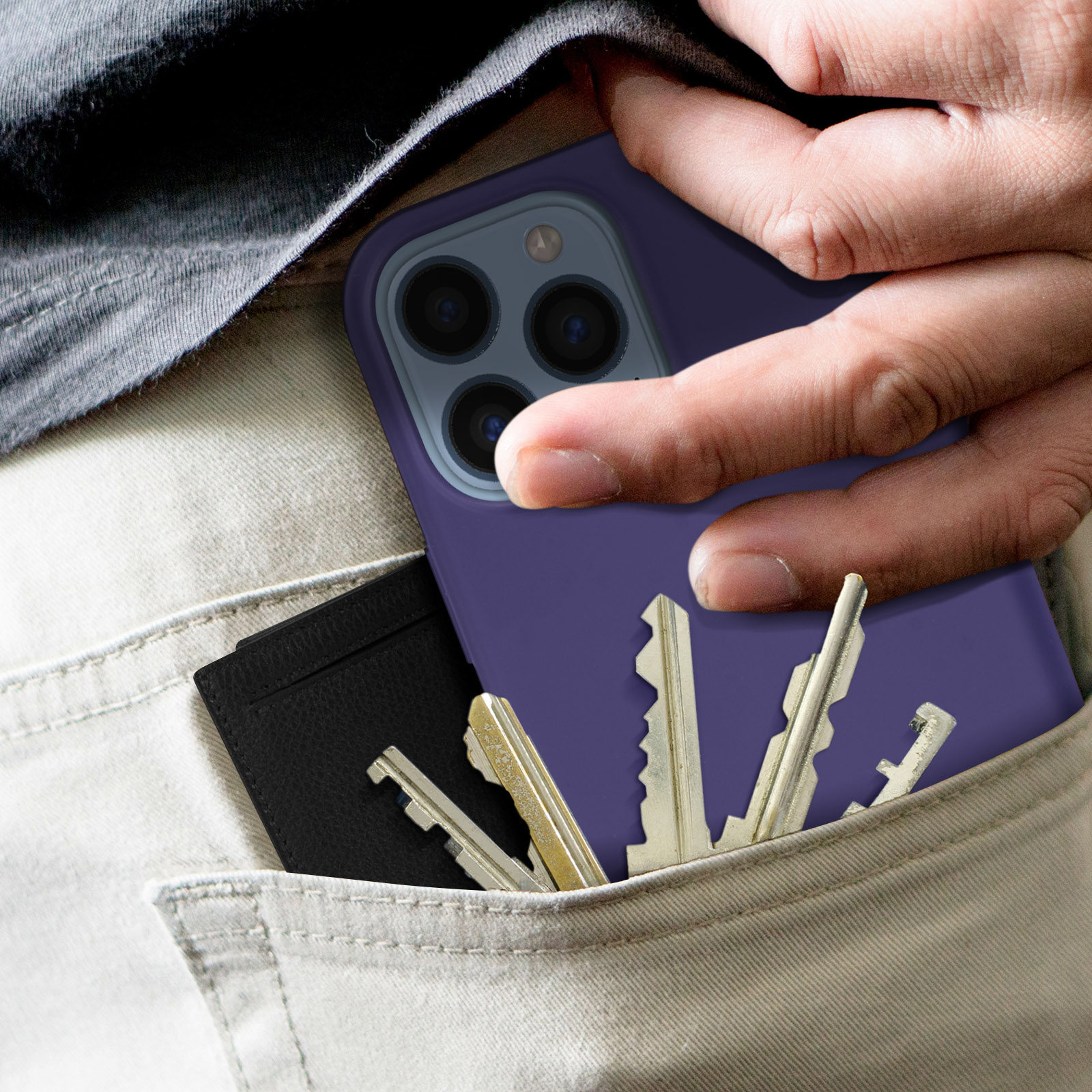 Main dans la poche avec une coque de téléphone violette et des clés. Un portefeuille noir est également visible.