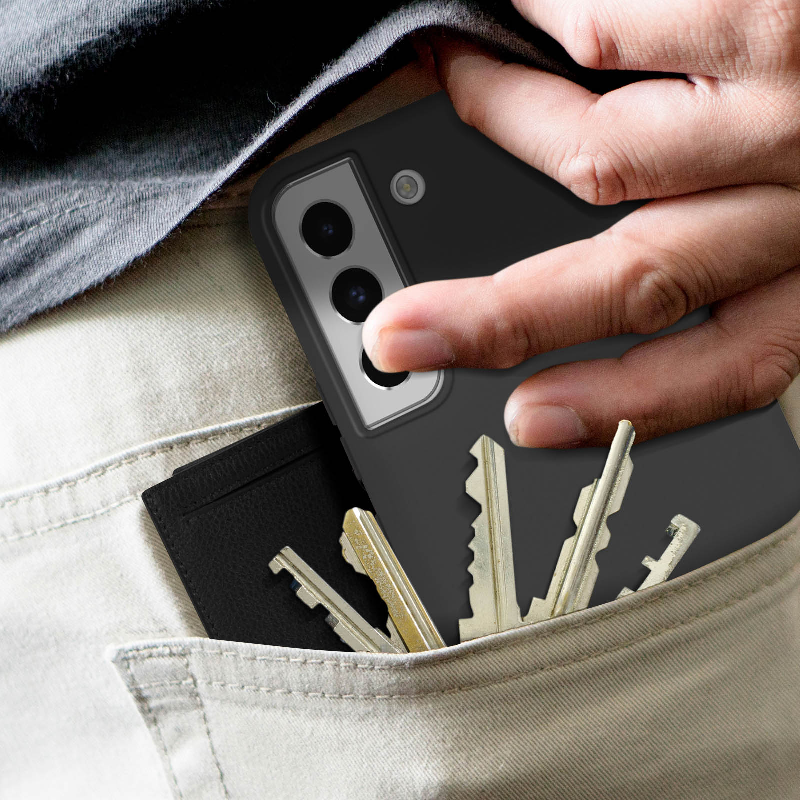 Hand in zak met sleutels en een telefoon. Telefoon zit in een zwart hoesje. Een zwarte portemonnee zit ook in de zak.