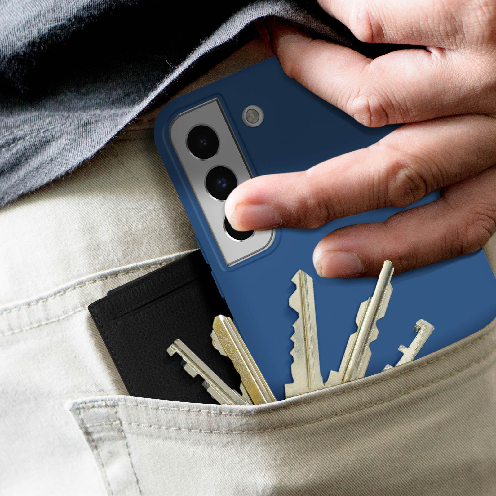 Een hand in een zak met een telefoonhoesje, sleutels en een portemonnee.