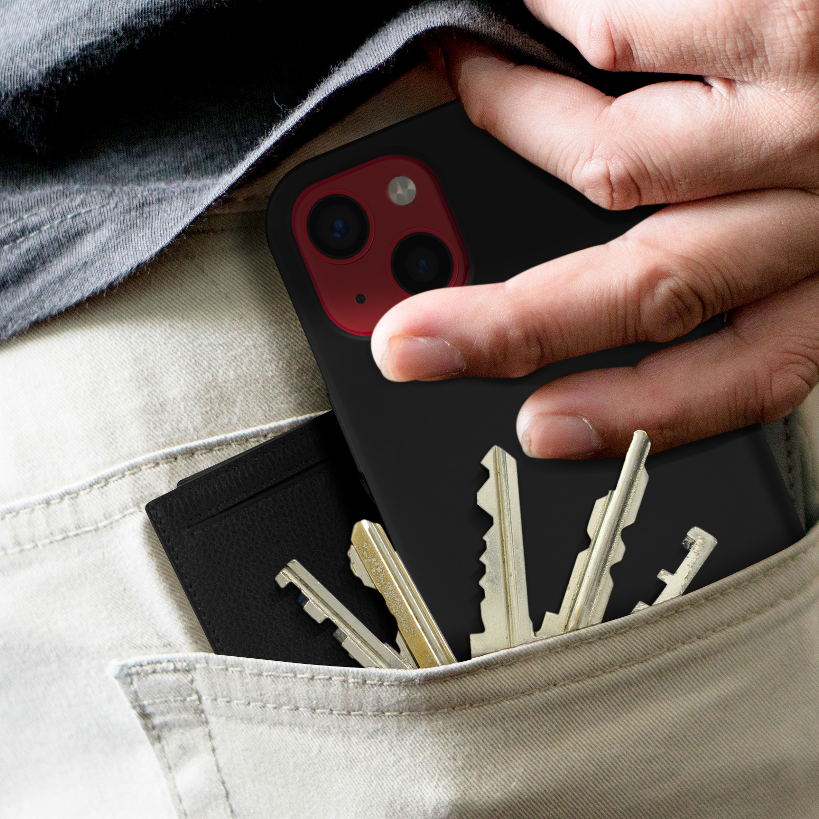 Hand die zwarte telefoon met hoes in zak steekt met sleutels en portemonnee.