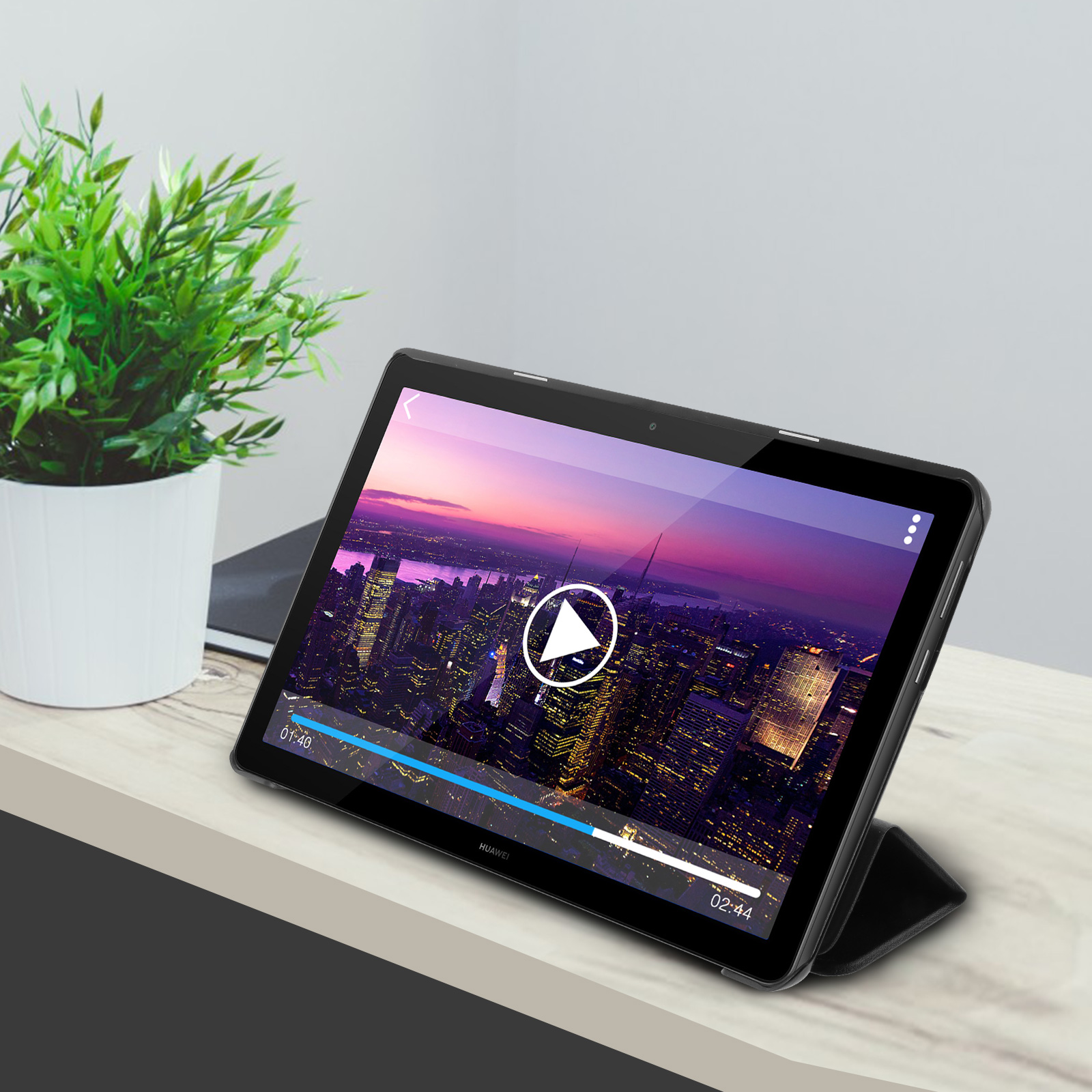 Tablet con video e sfondo urbano. Pianta a sinistra. Tablet con custodia nera, su superficie in legno.