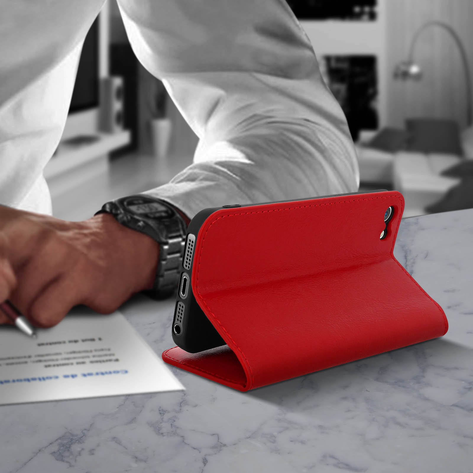 Custodia rossa per telefono su un tavolo. Una persona sta scrivendo su un foglio.