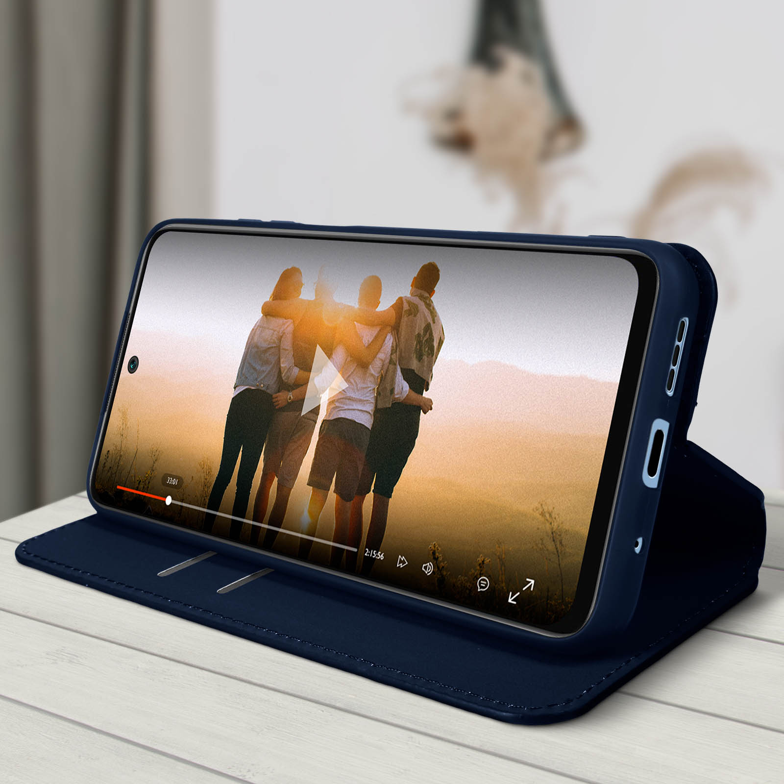 Téléphone affichant une vidéo avec des personnes. Téléphone dans un étui marine sur une table en bois. Flou.
