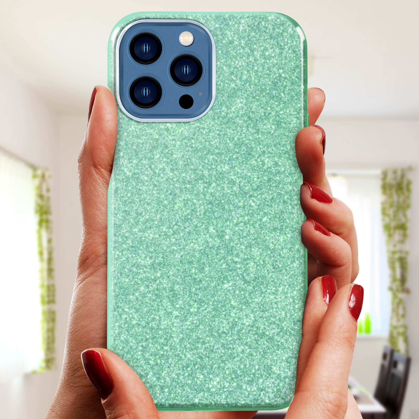 Mani che tengono una custodia verde glitterata. Smalto rosso. Sfondo sfocato, tonalità verde.