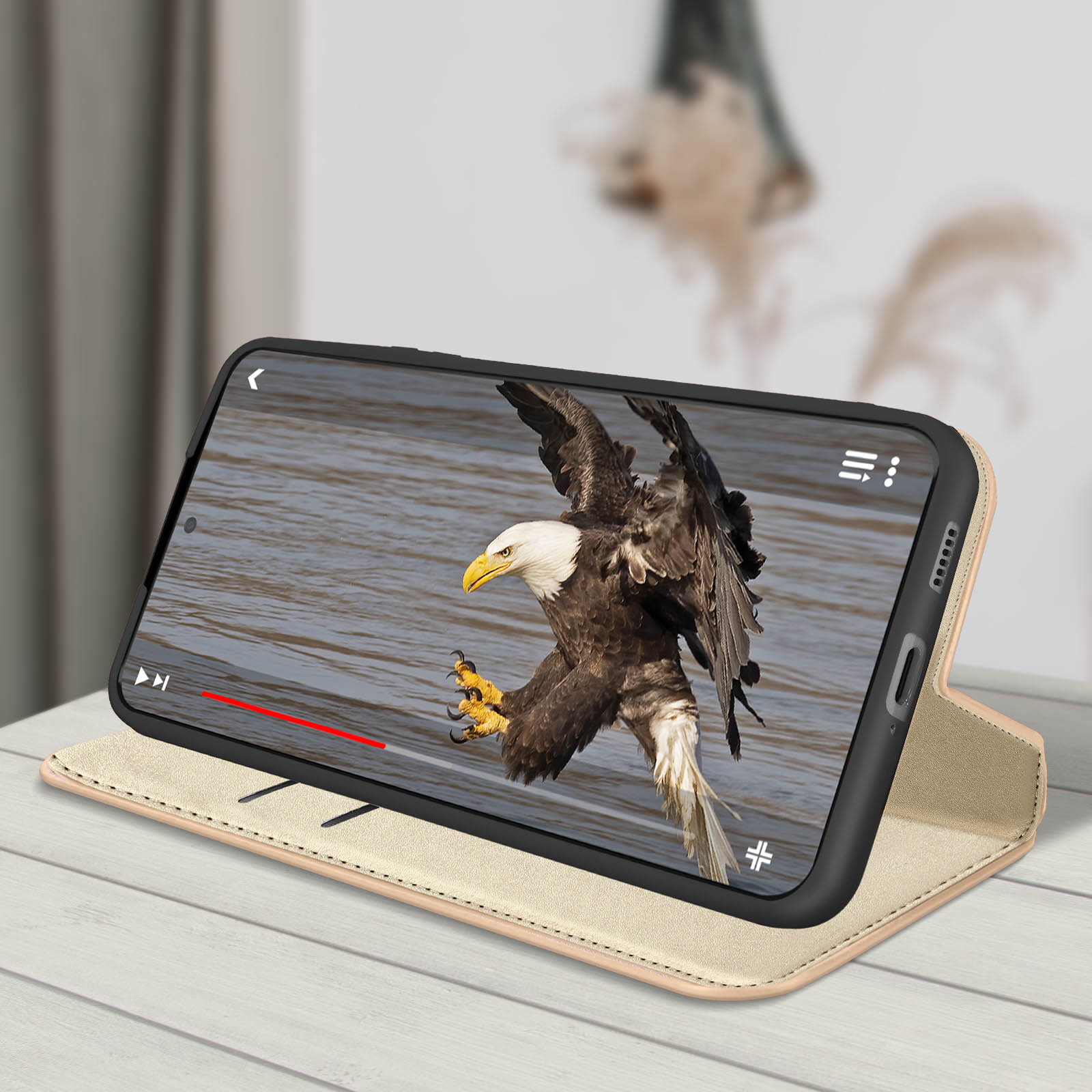 Telefono in una custodia marrone chiaro riproduce un video di un'aquila calva in volo. Si appoggia su una superficie chiara.