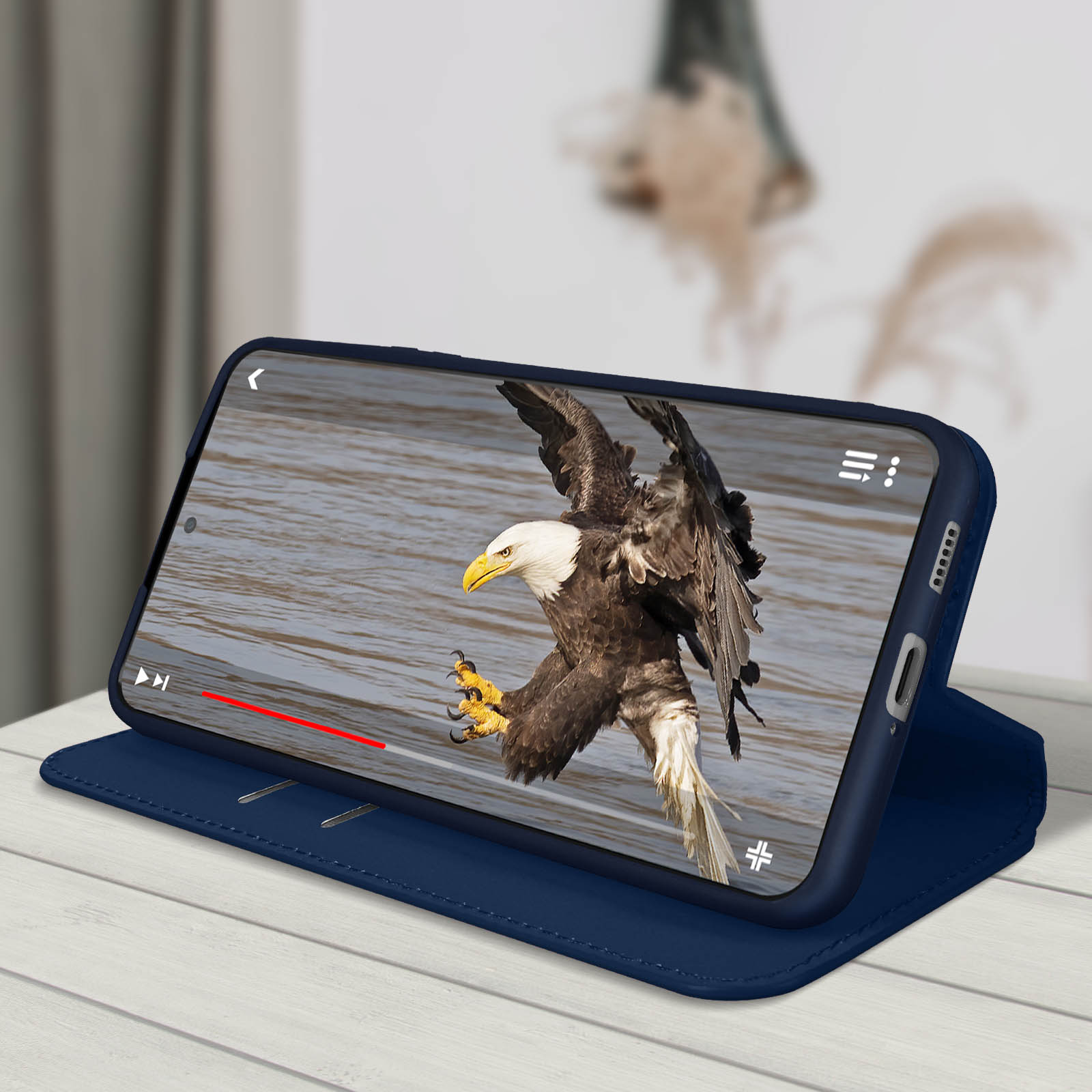 Telefoon in een blauwe hoes die een video van een adelaar toont. Wit oppervlak.