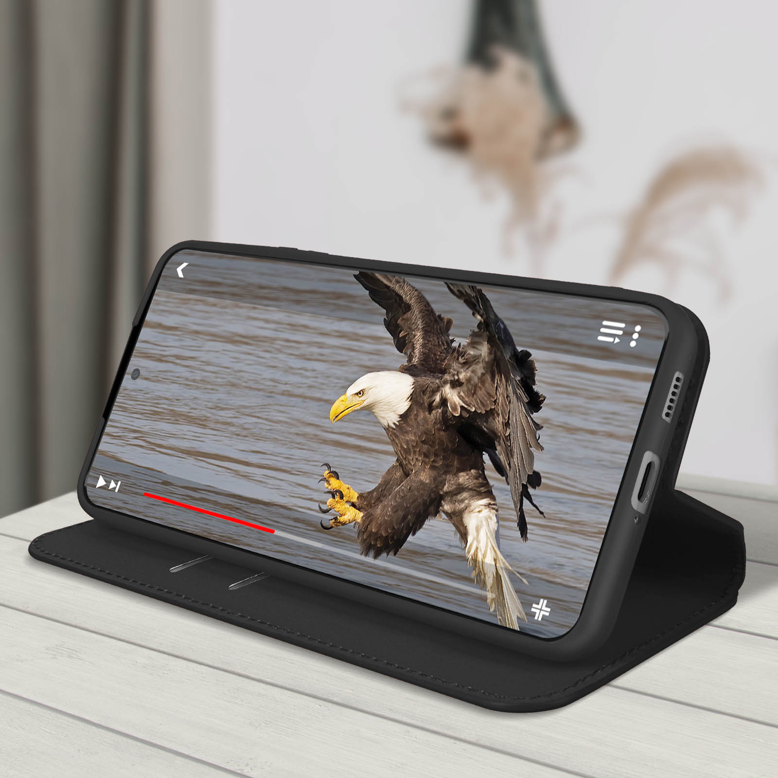 Téléphone dans un étui noir montrant une vidéo d'un aigle. Surface blanche.