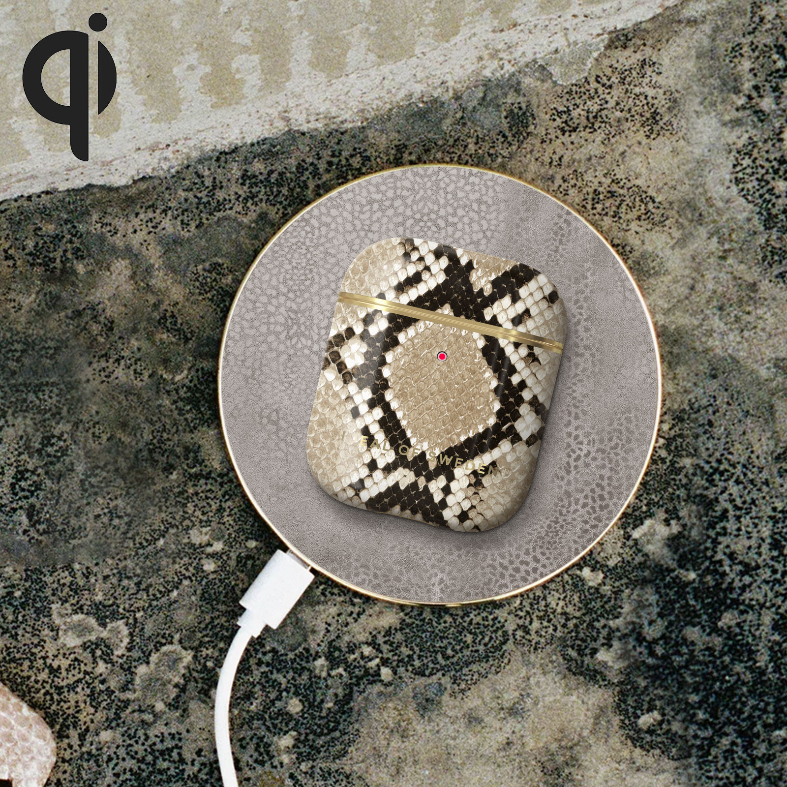 Una base de carga con una funda de AirPod con estampado de piel de serpiente. Un cable blanco conectado.