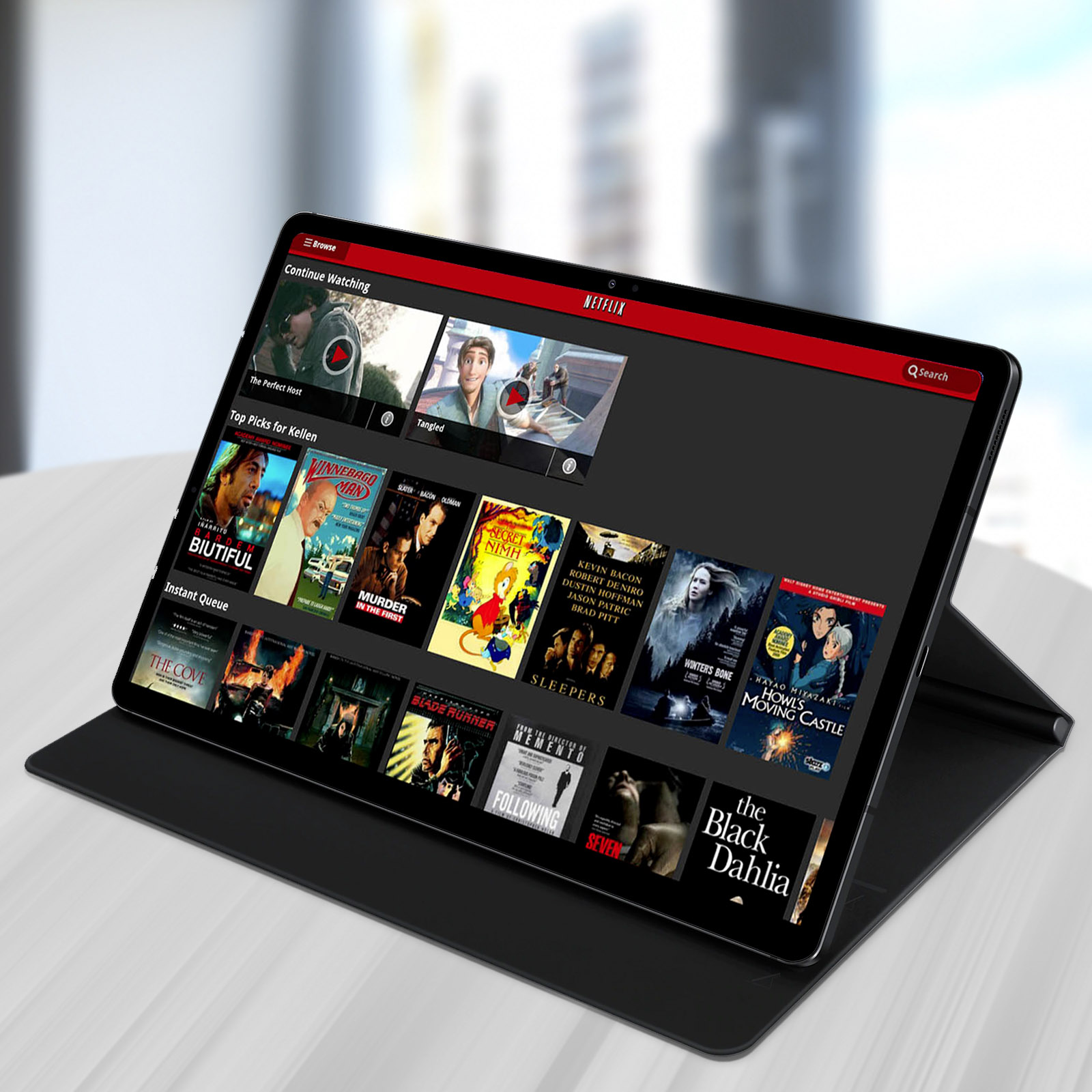 Tableta mostrando la interfaz de Netflix. Tableta negra con una cubierta negra. Superficie blanca.